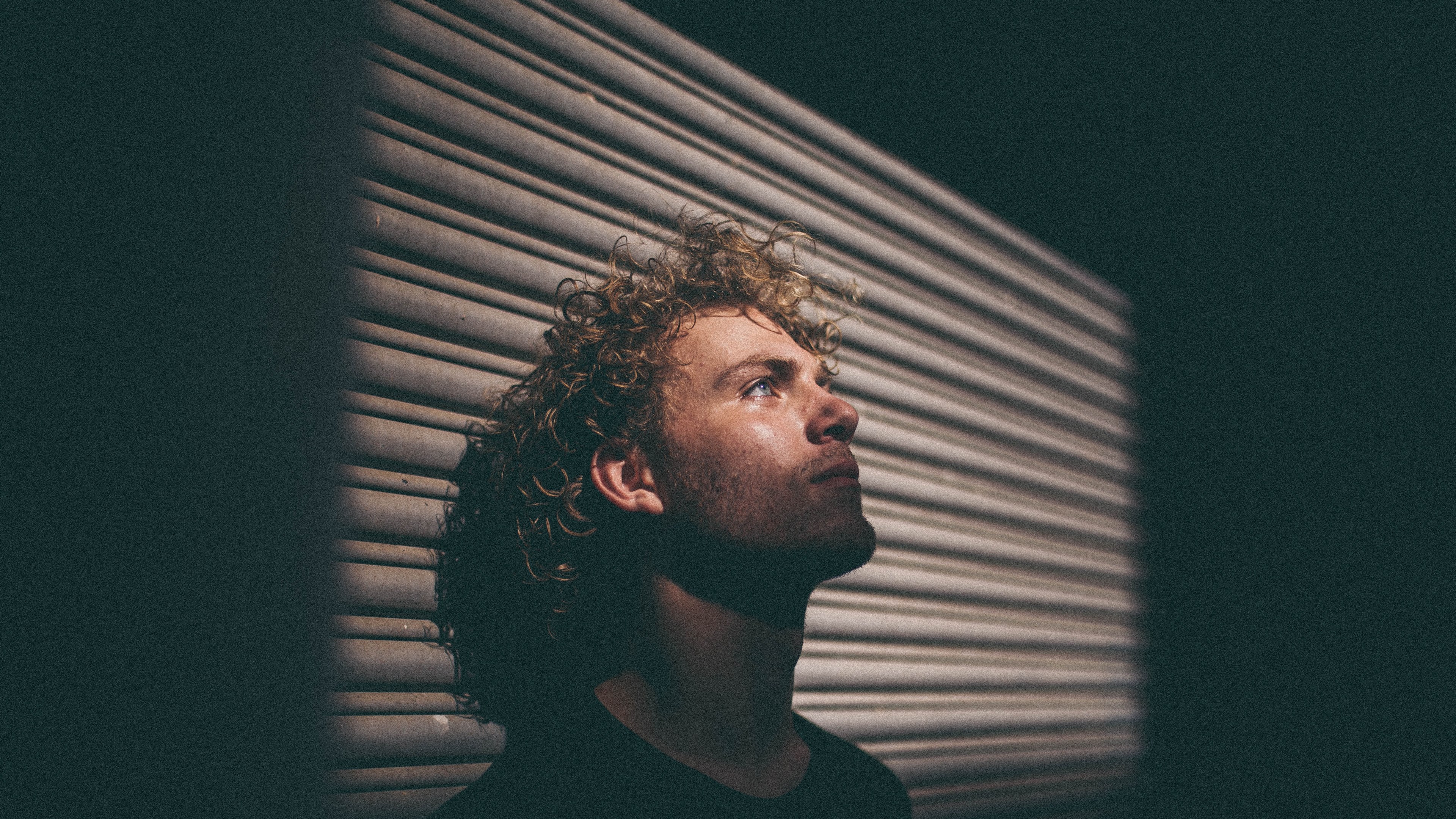 Wallpaper / a man with curly hair in shadow leans his head back against a wall, man leaning head on wall 4k wallpaper free download