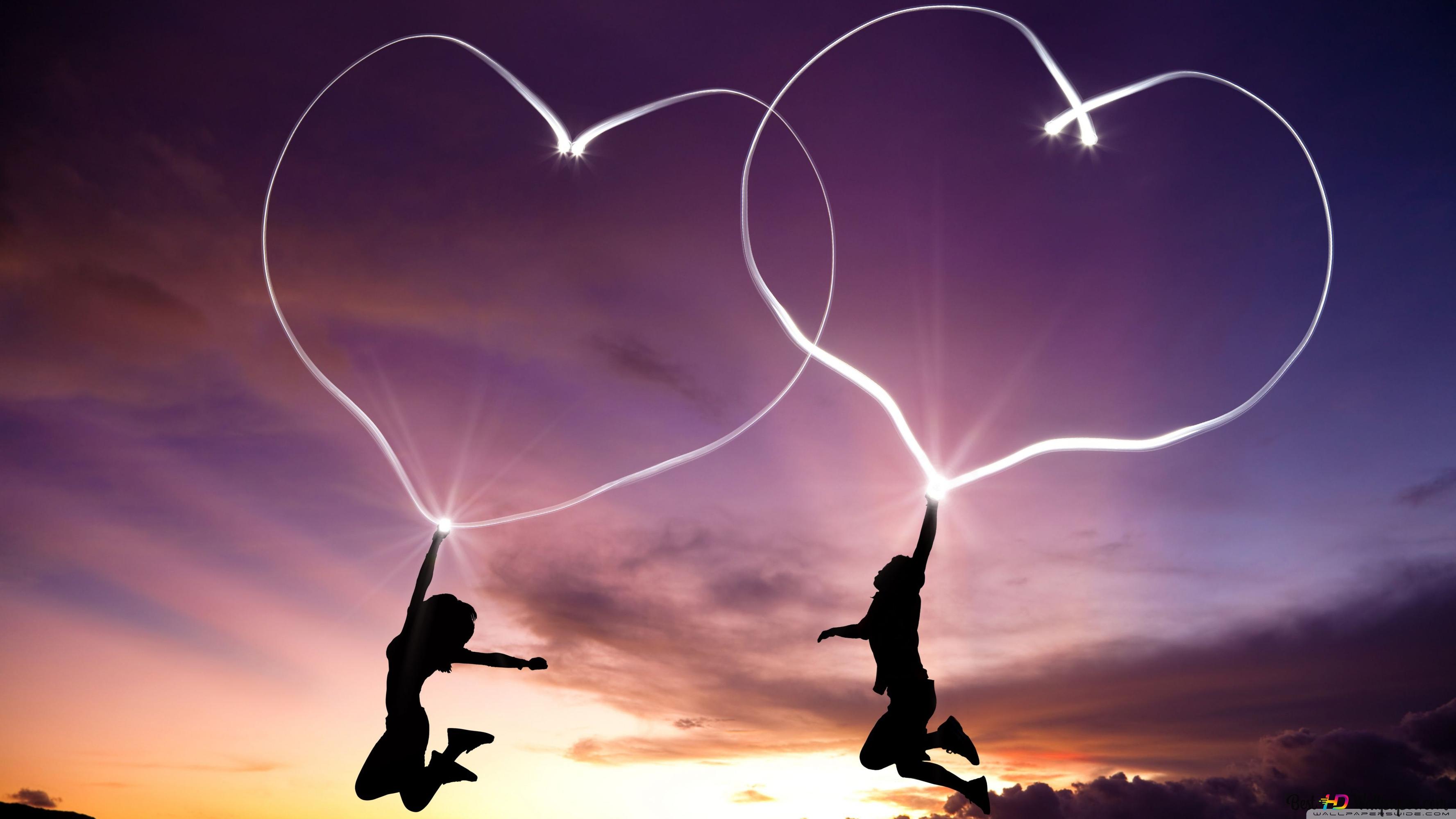 Lovers at sunset and a heart of light in their hands 4K wallpaper download