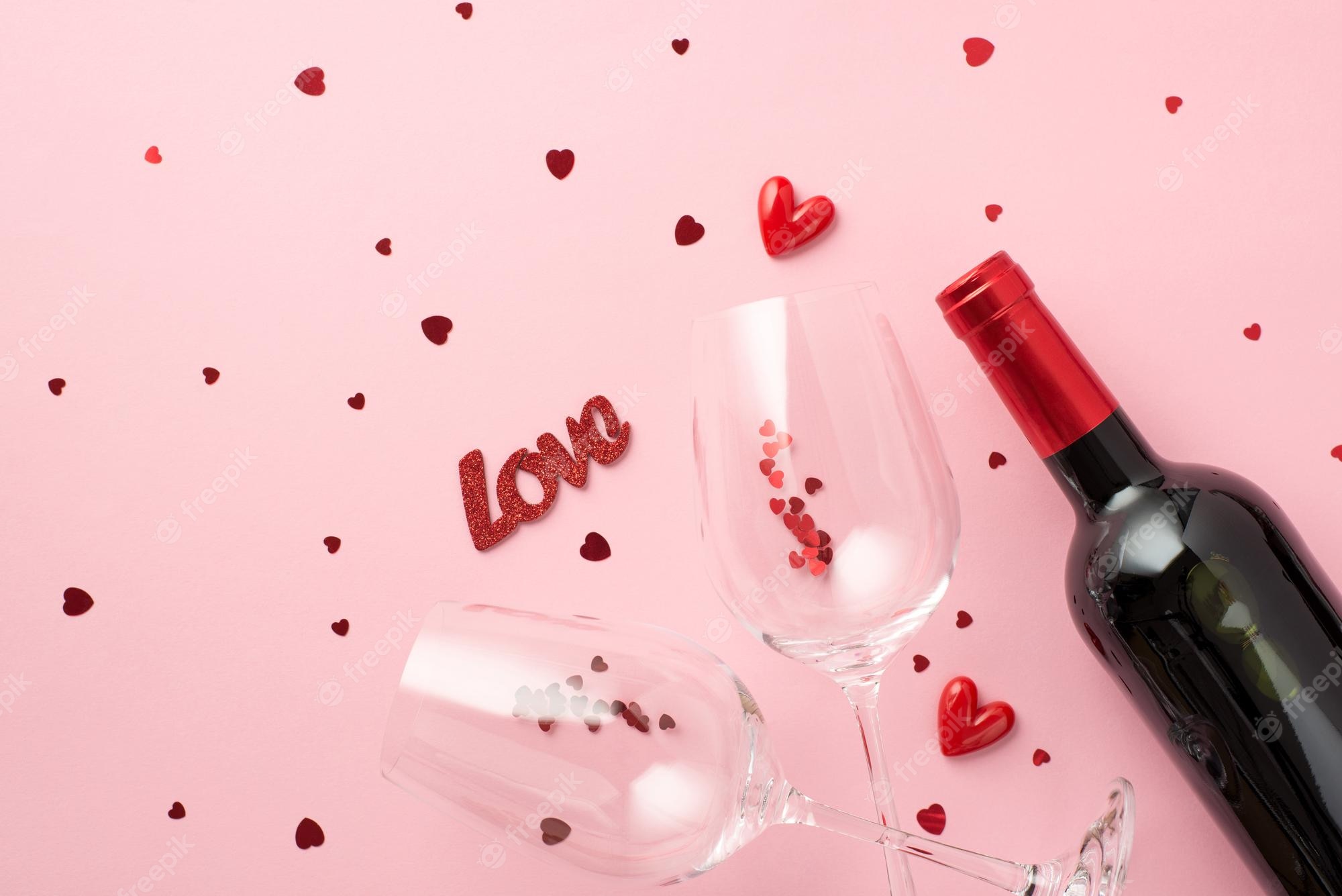 Premium Photo. Top view photo of saint valentine's day decorations inscription love small hearts two wineglasses with heart shaped confetti and wine bottle on isolated pastel pink background