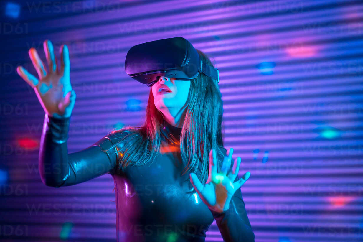 Young woman in VR headset gesticulating and interacting with virtual reality under neon illumination