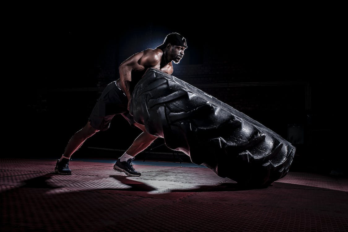 Strong shirtless black man flipping heavy tire in dark gym · Free