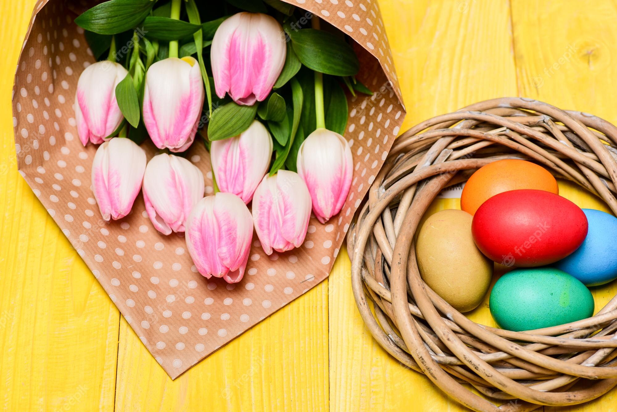 Premium Photo. Tradition celebrate easter happy easter season easter is coming collecting easter eggs spring vibes colorful eggs and bouquet fresh tulip flowers on yellow table background spring holiday