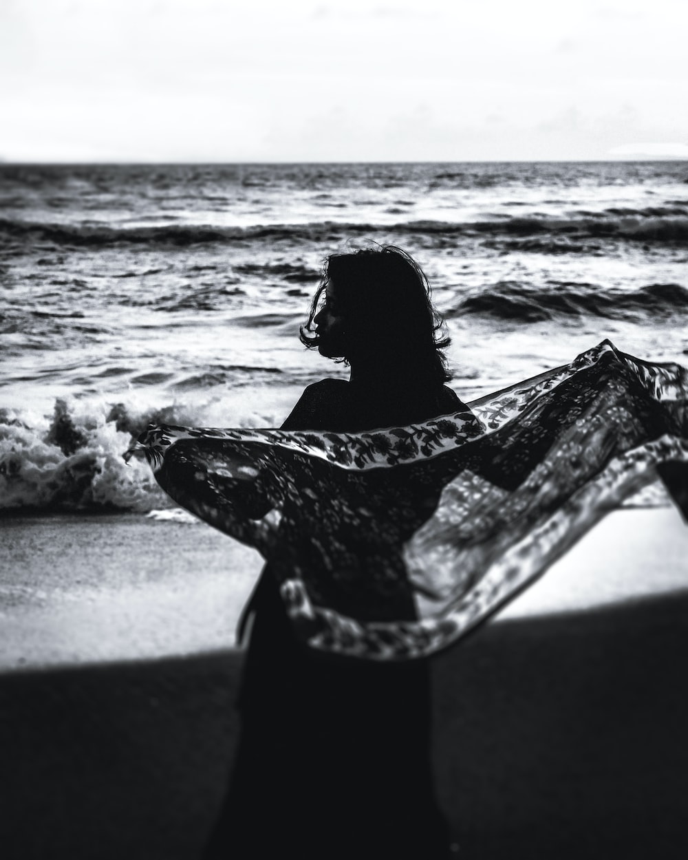 grayscale photo of woman in black and white dress carrying surfboard on beach photo