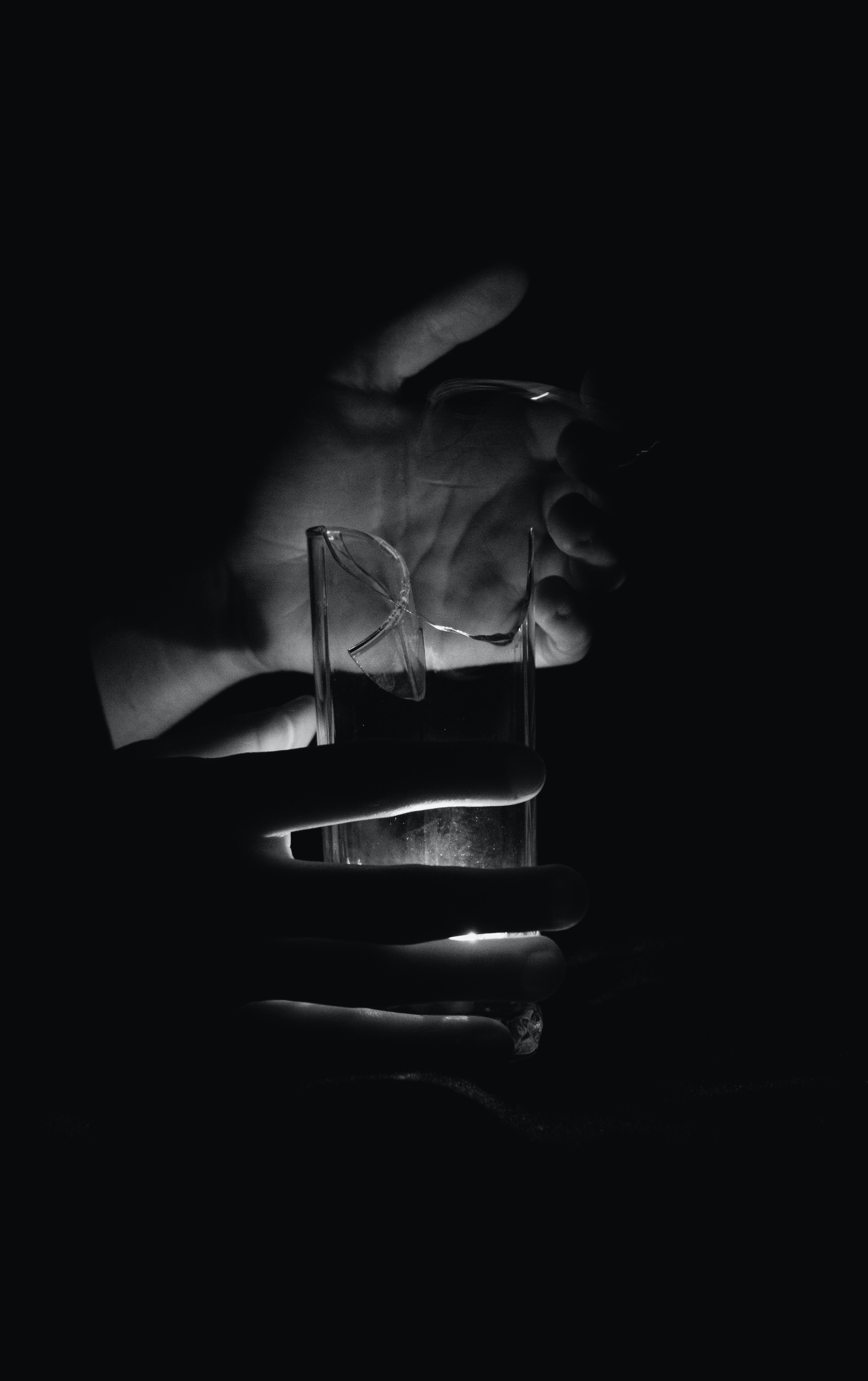 Grayscale Photo of Person Holding a Broken Glass in the Dark · Free