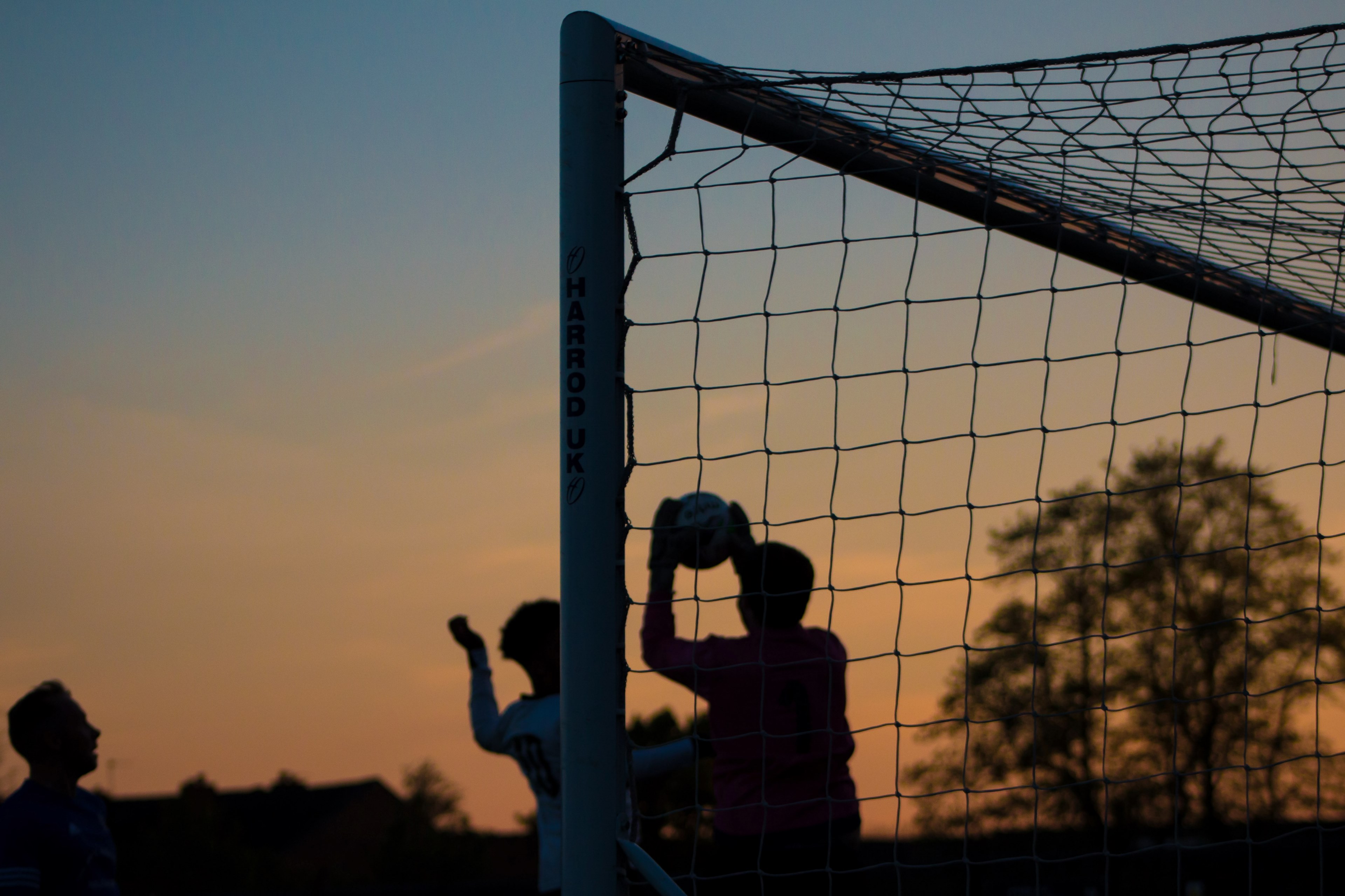 Wallpaper / three children play soccer at sunset at ewen fields, silhouette goalkeeper catching the ball 4k wallpaper free download