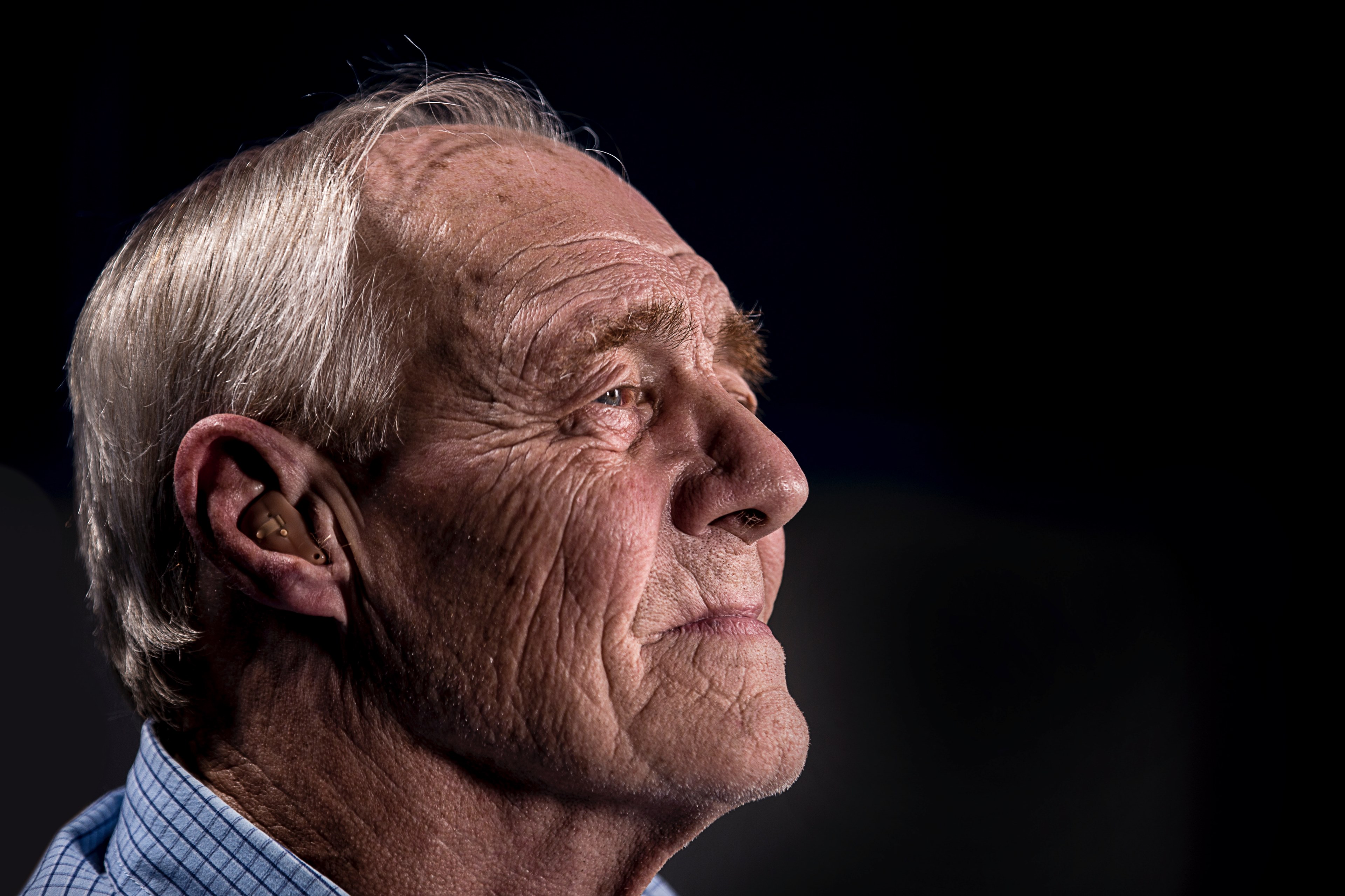 Wallpaper / old man with wrinkle face and gray hair looking out and using a hearing aid, old man with hearing aid_ 4k wallpaper free download