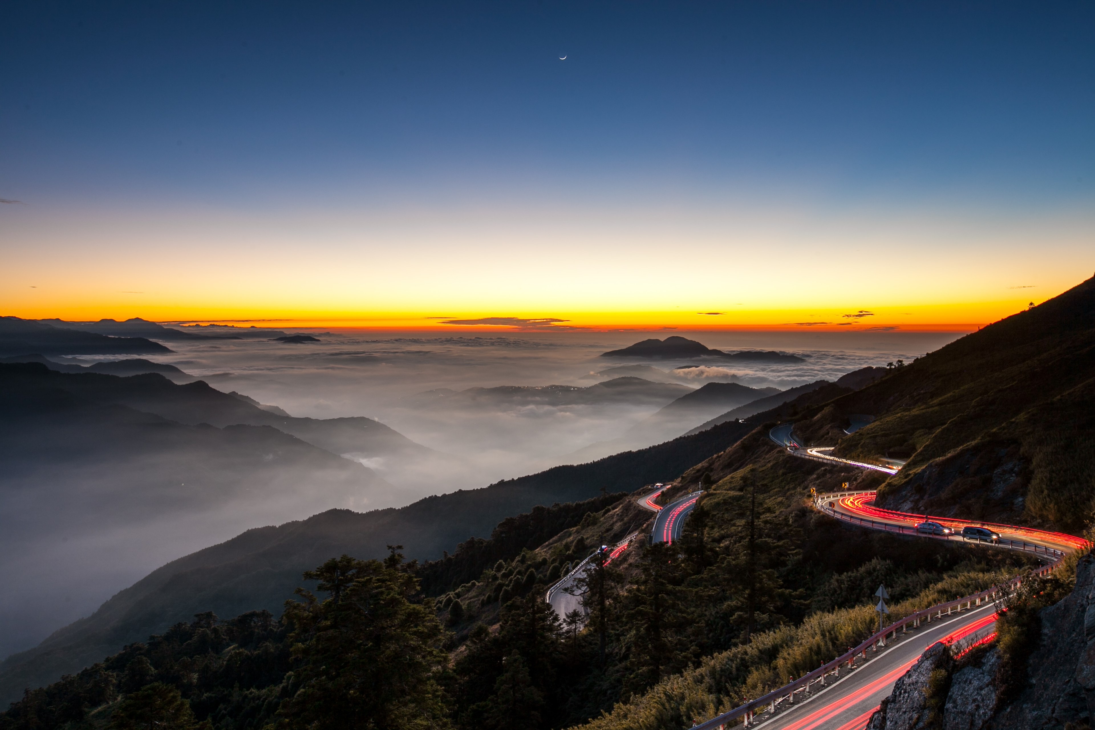 Wallpaper / a colorful sunset and streaks of headlights on a mountainside highway, mountain highway 4k wallpaper free download