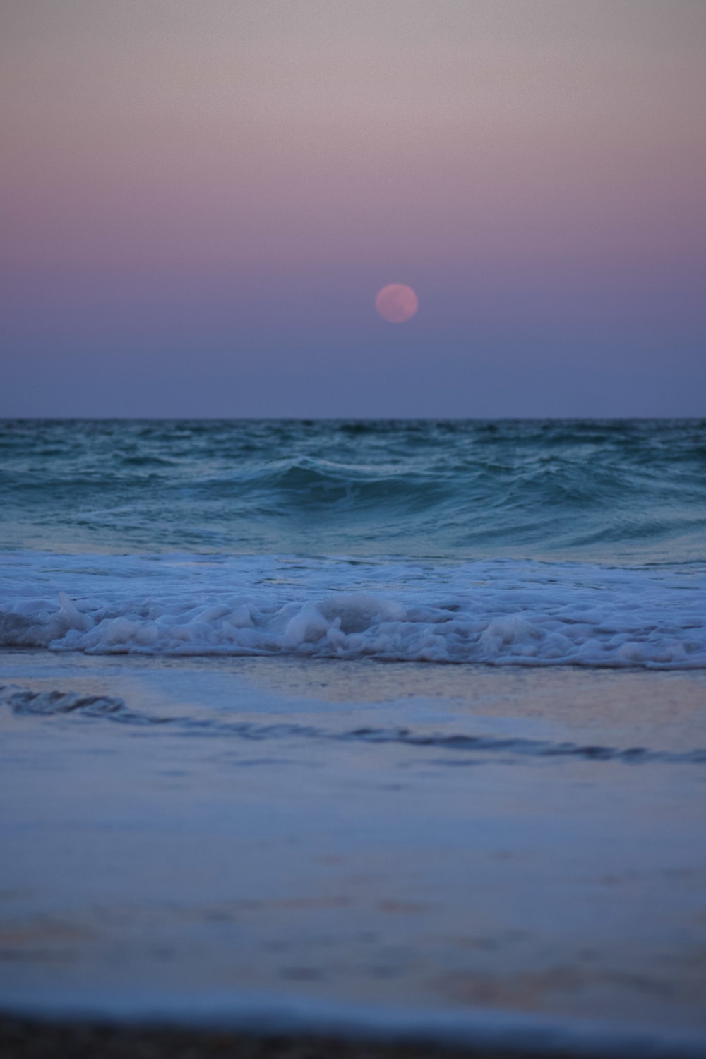 Ocean waves crashing on shore during sunset photo