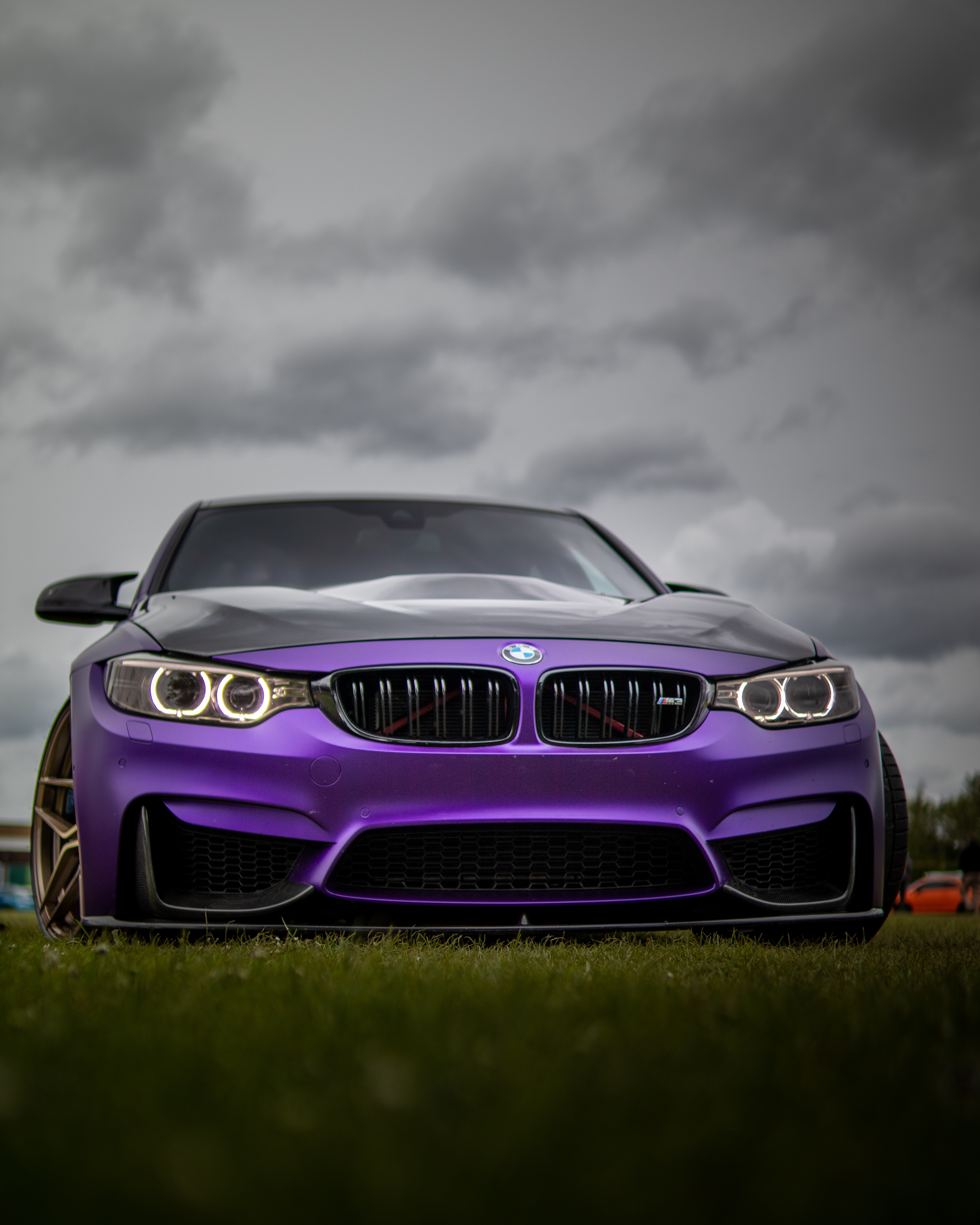 A Purple Bmw On Grass Under Dark Clouds