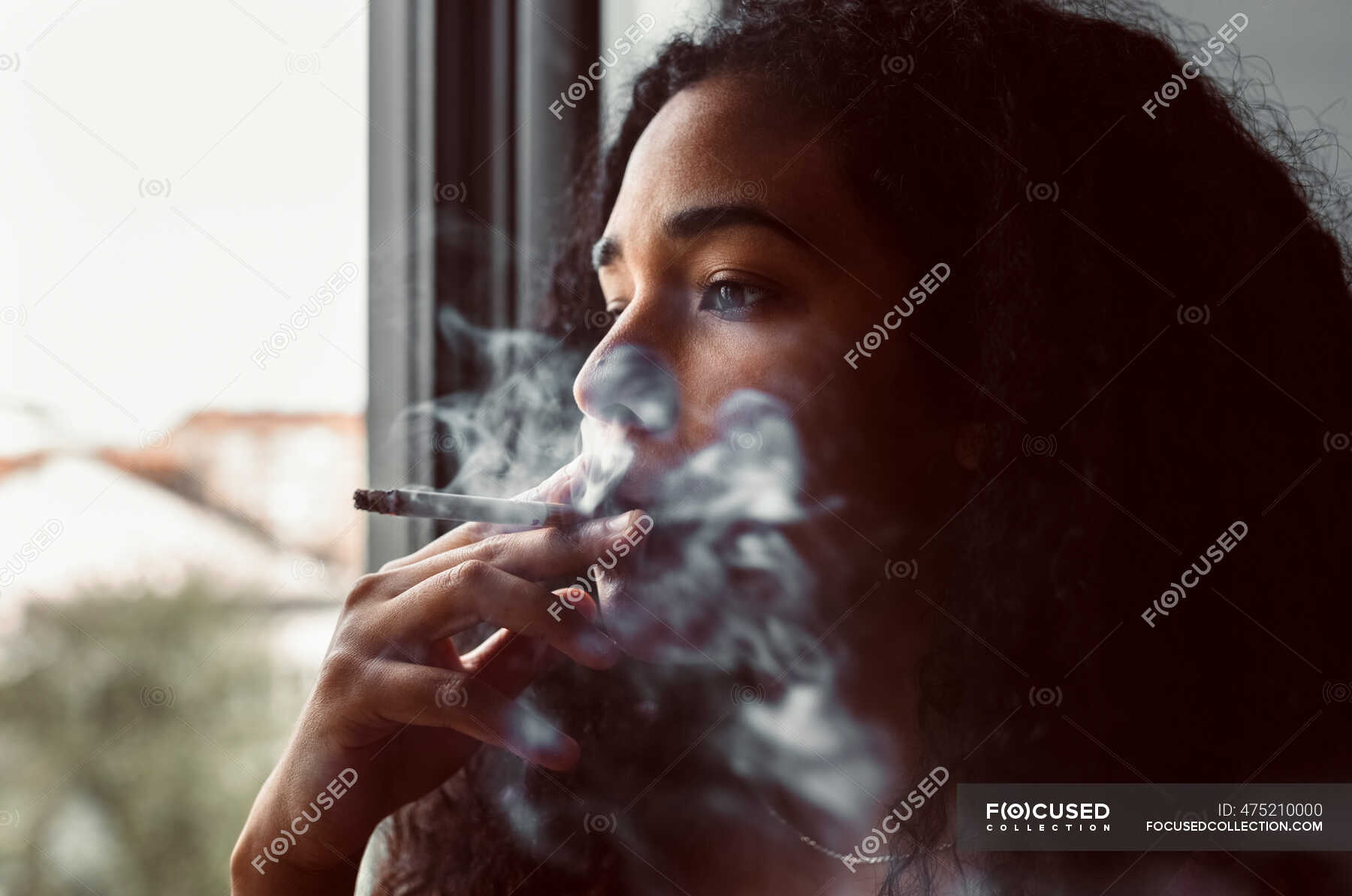 Portrait of young woman smoking a cigarette at the window