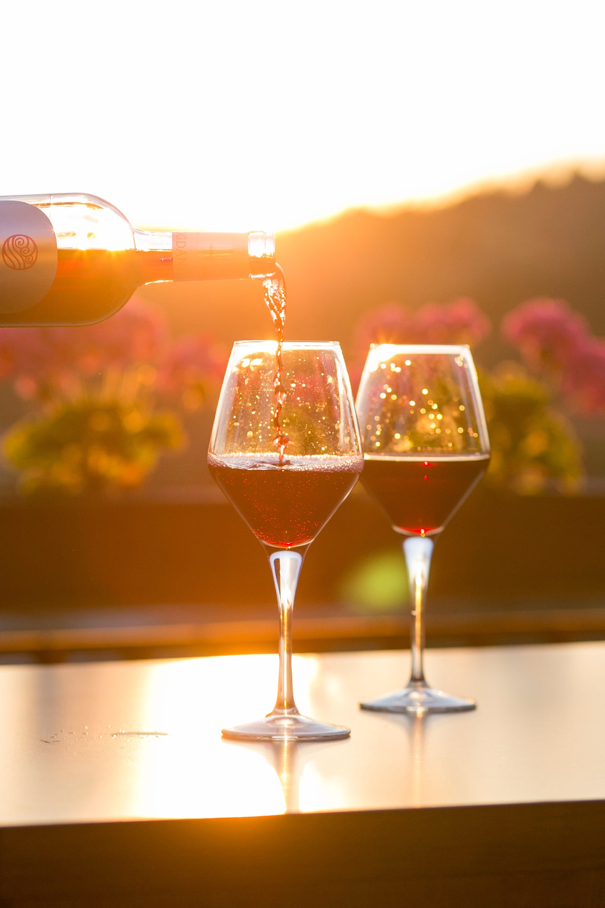 Wallpaper / a person pouring red wine into one of two glasses with flowers and the setting sun in the background, sunset and wine 4k wallpaper free download