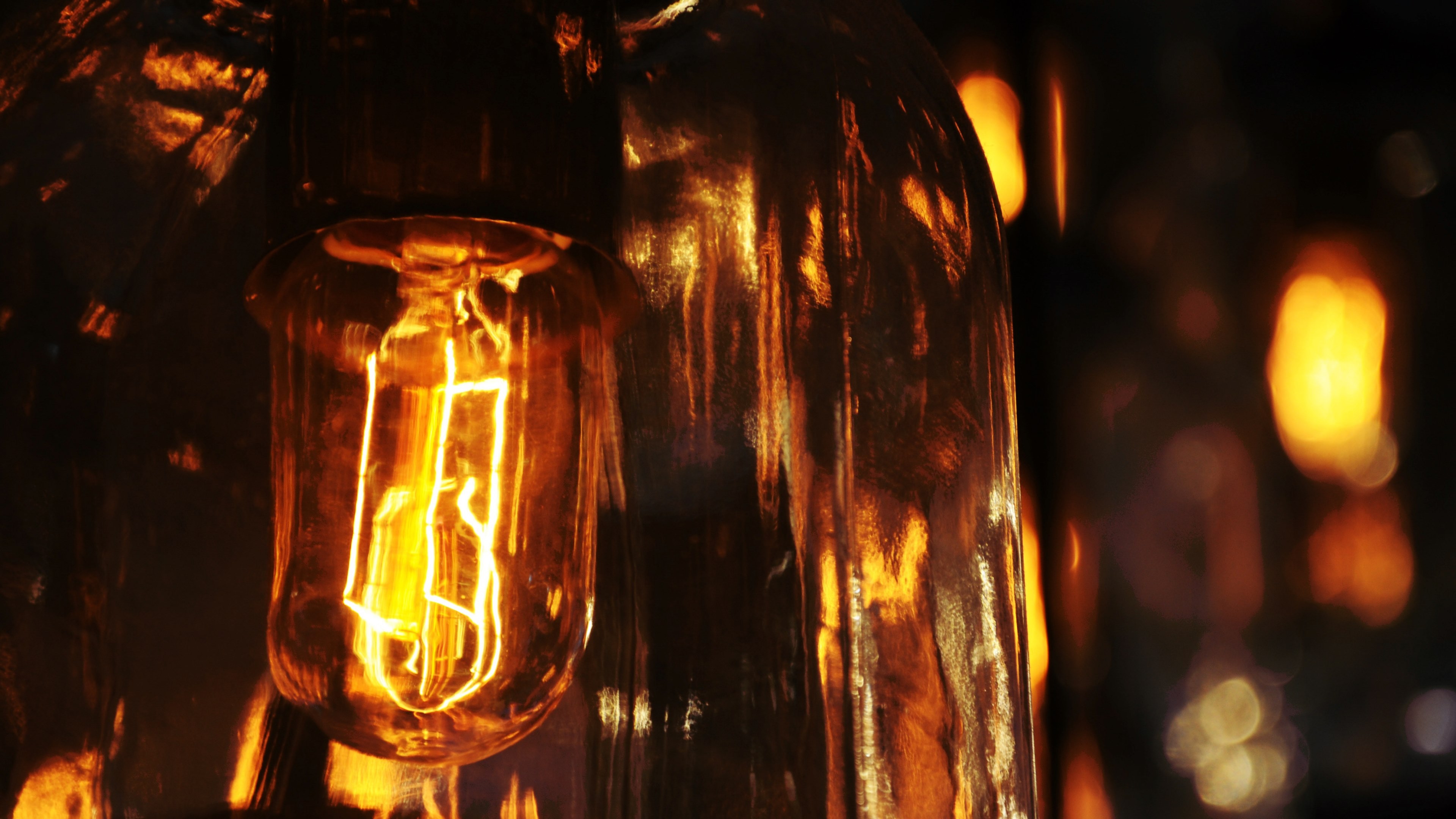 Wallpaper / the fillaments of a lightbulb emitting a warm glow and reflecting in the glass of the bulb, lightbulb reflections 4k wallpaper free download