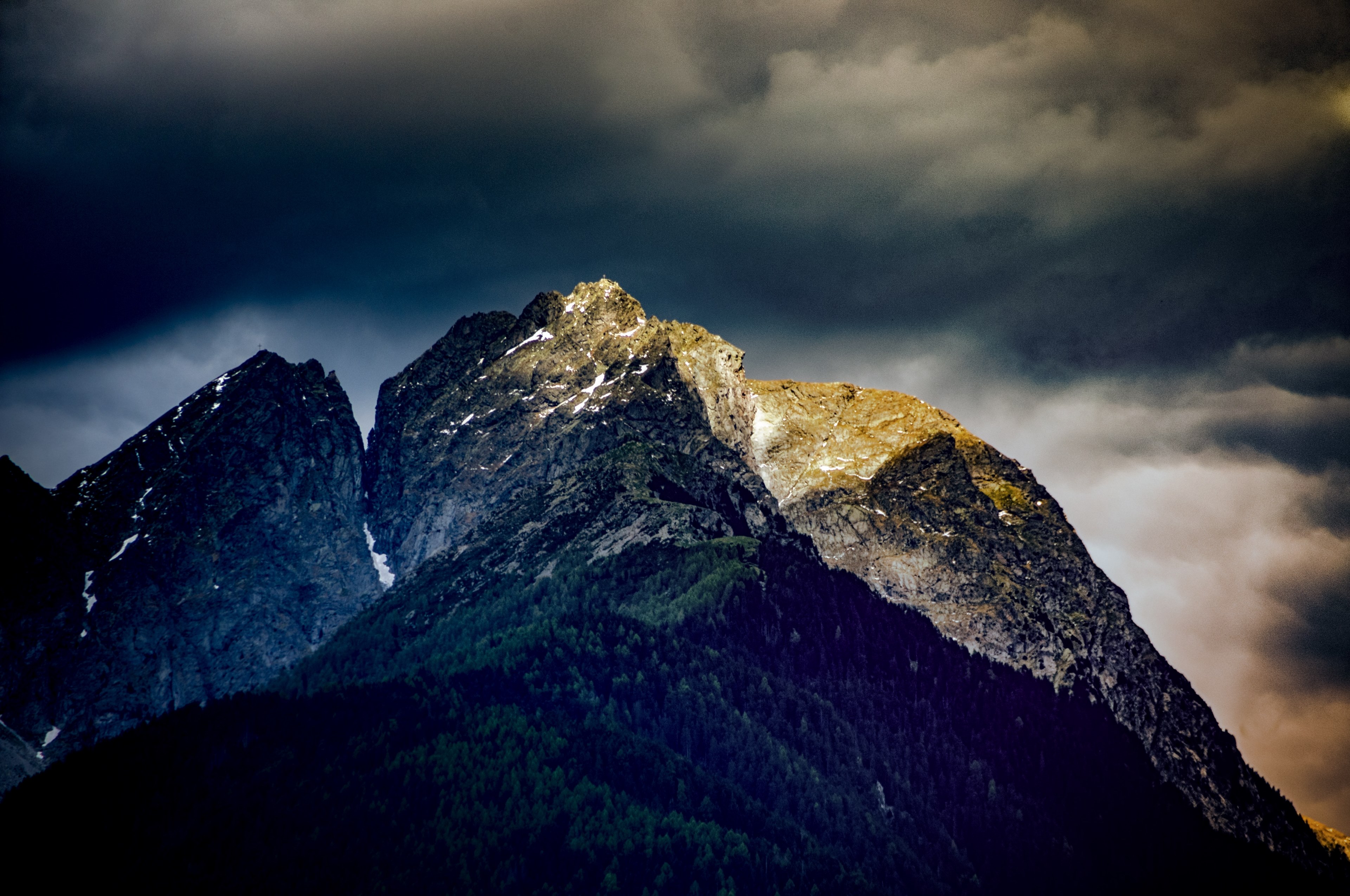 Wallpaper / a dramatic view of a mountain illuminated by rays of light under thick gray clouds, dark mountains 4k wallpaper free download