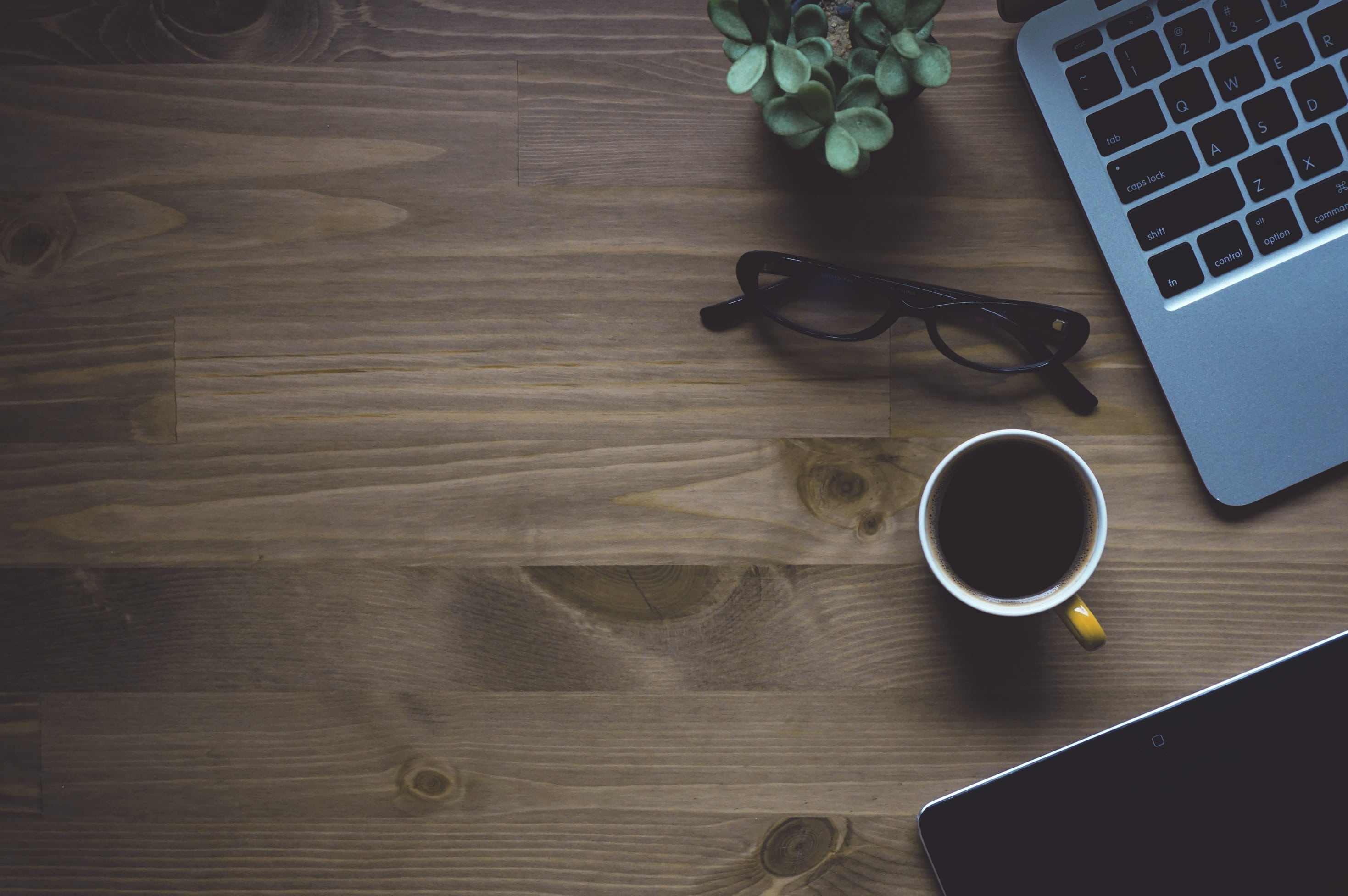 White Ceramic Mug Near Eyeglasses With Black Frames And Gray Laptop Computer On Brown Table Wallpaper