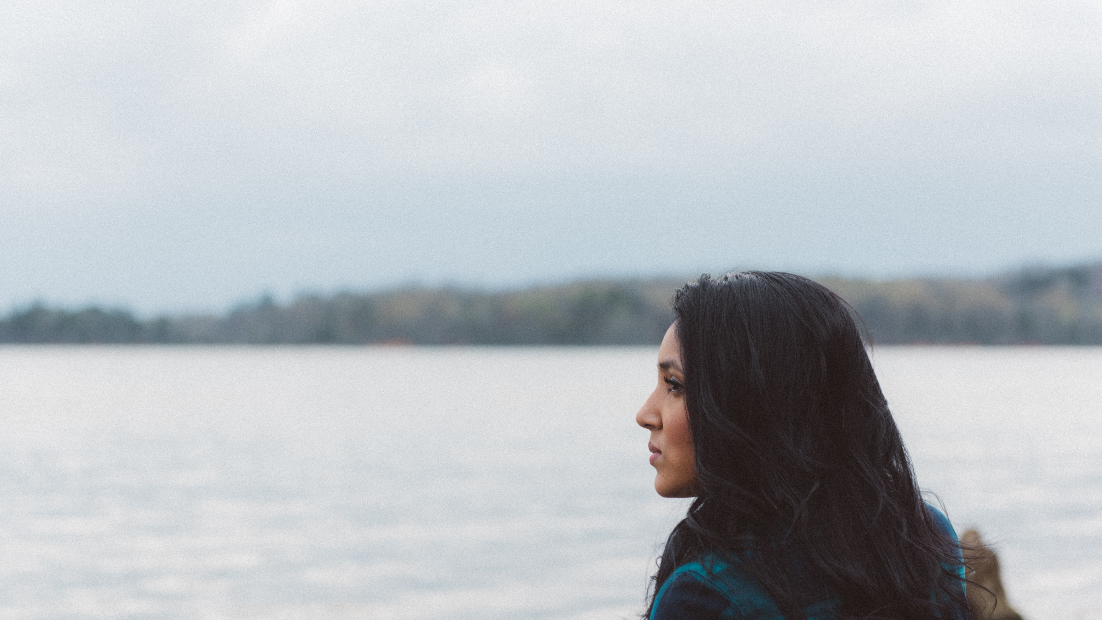 Wallpaper / woman standing alone on a lake shore thinking, clearing her head 4k wallpaper free download