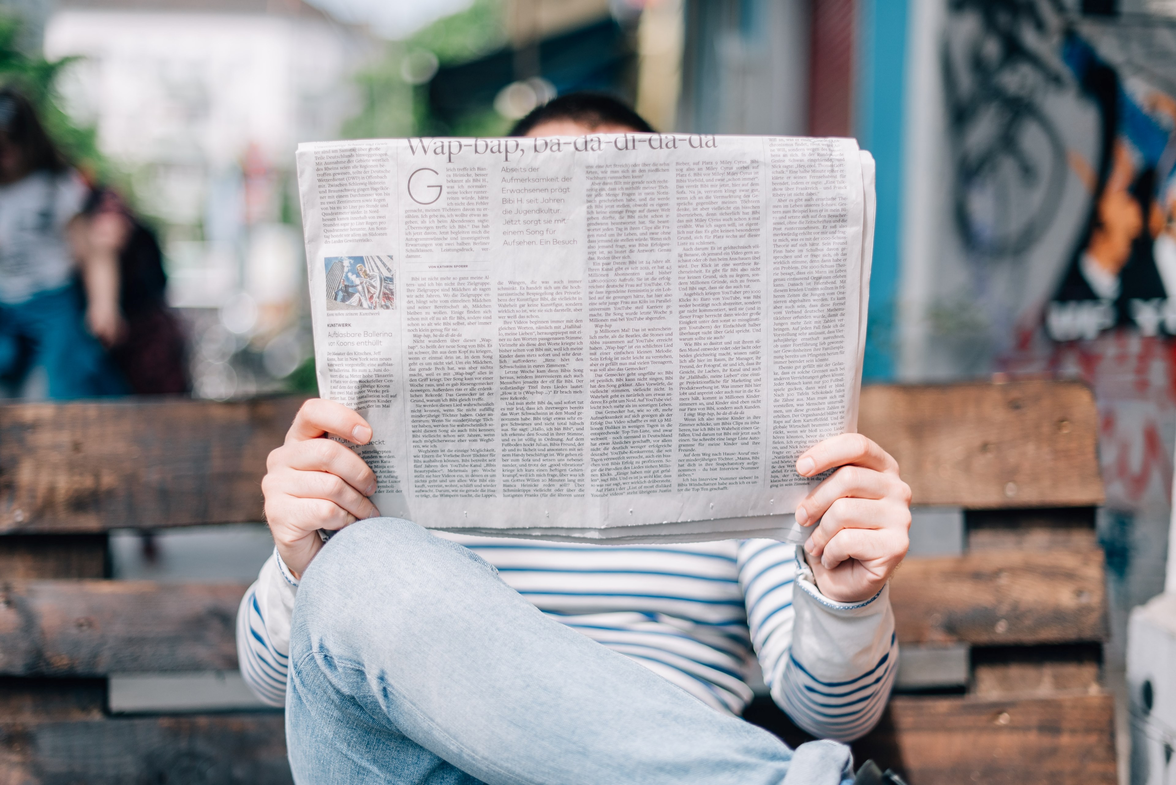 Wallpaper / a person reads a newspaper on a bench in front of a graffitied building in berlin, person reading a newspaper 4k wallpaper free download