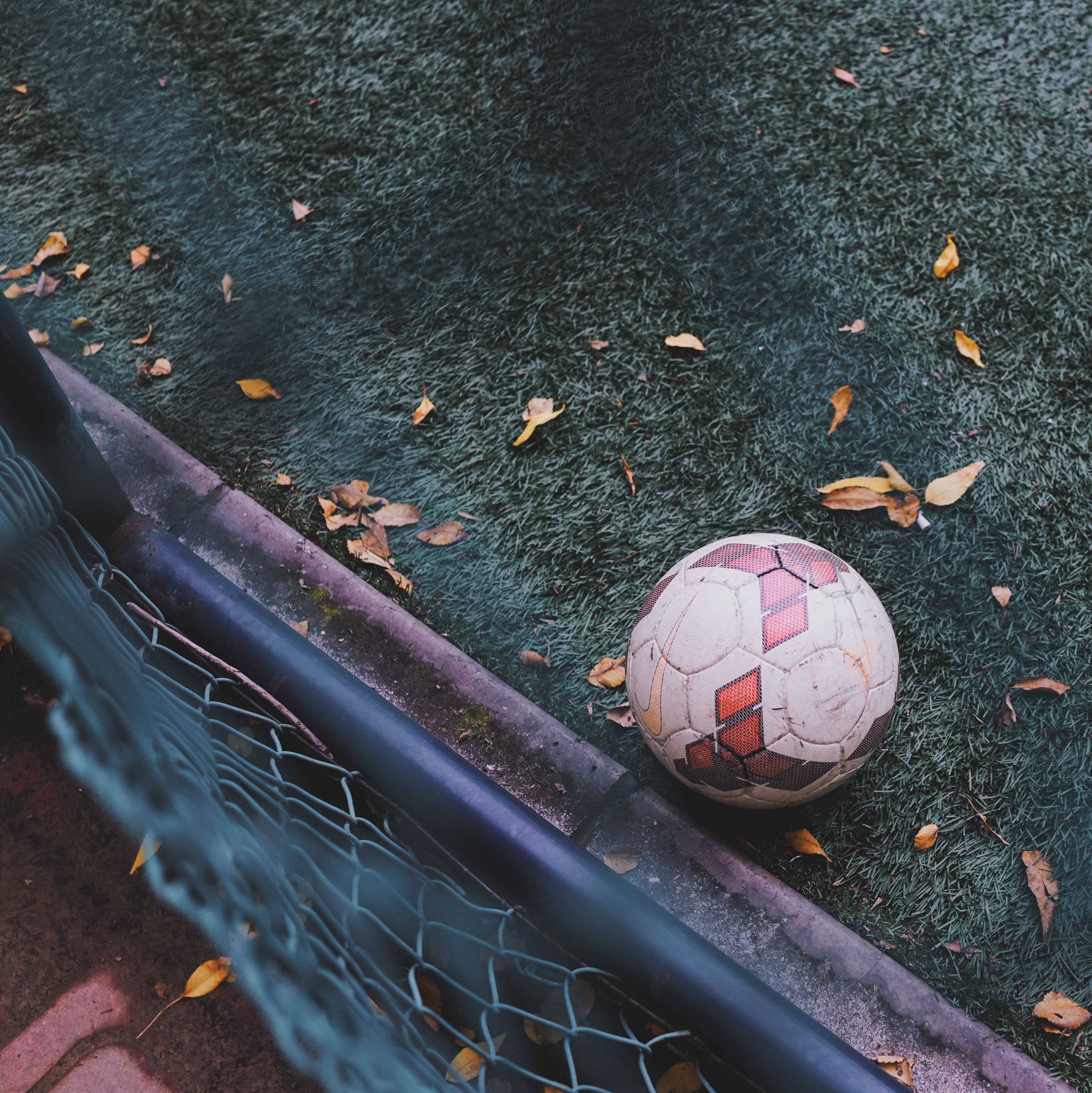 Wallpaper / view over the fence on the soccer ball sitting on a green turf pitch, football on fall ground 4k wallpaper free download