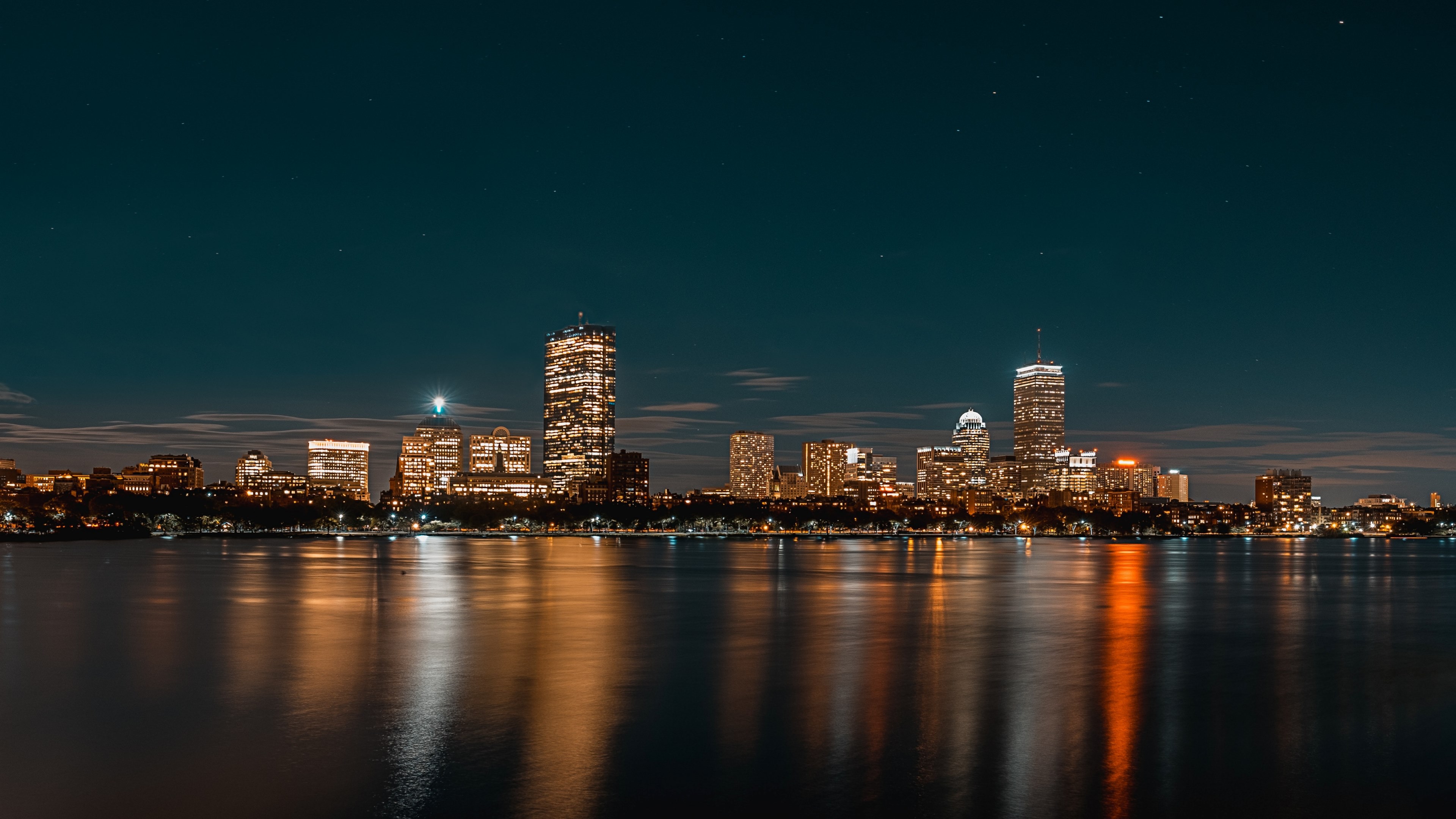 Wallpaper / a bright skyline with a city waterfront seen from the water at night, bright skyline over water 4k wallpaper free download
