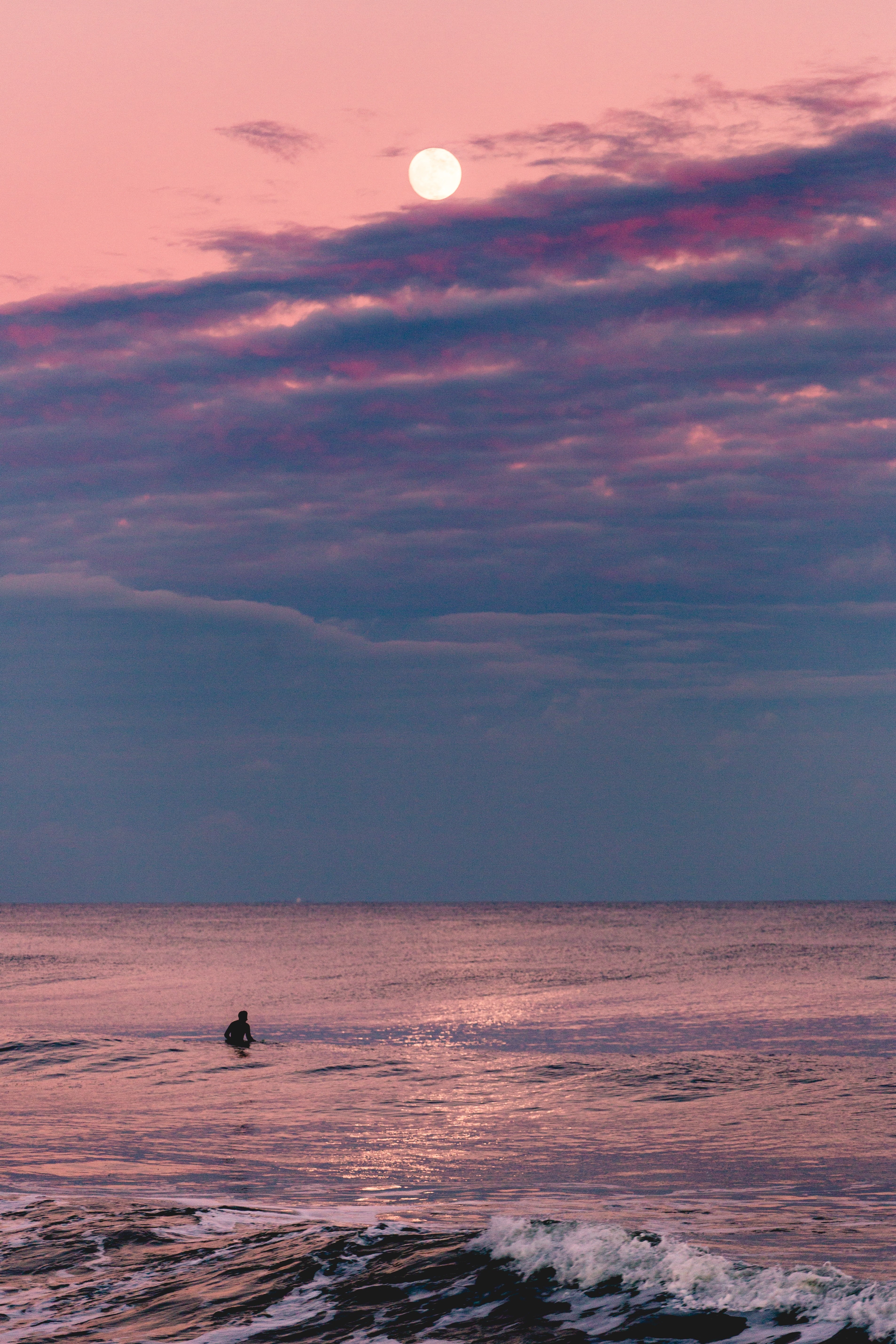 Wallpaper / a surfer at avon by the sea at dusk with a full moon above on a pink cloudy sky, not afraid of sharks 4k wallpaper free download