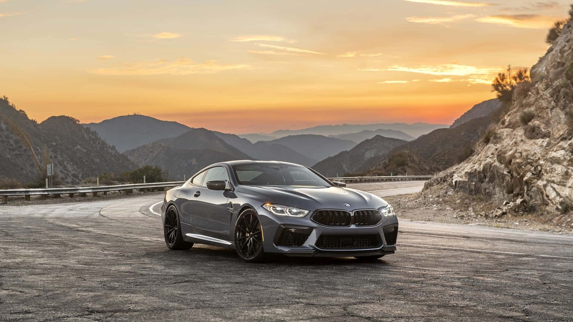 Download The Bmw M8 Is Driving Down A Mountain Road At Sunset Wallpaper