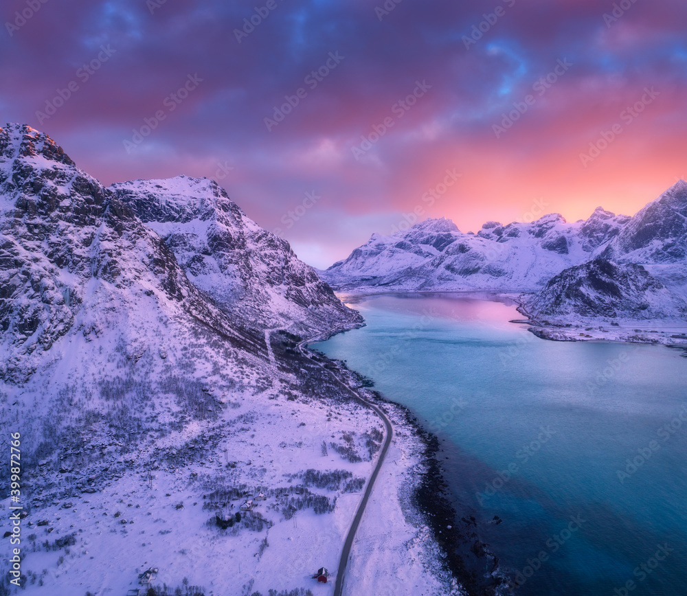 Aerial view of beautiful snowy mountains, sea, road, sky with pink clouds at sunset in winter