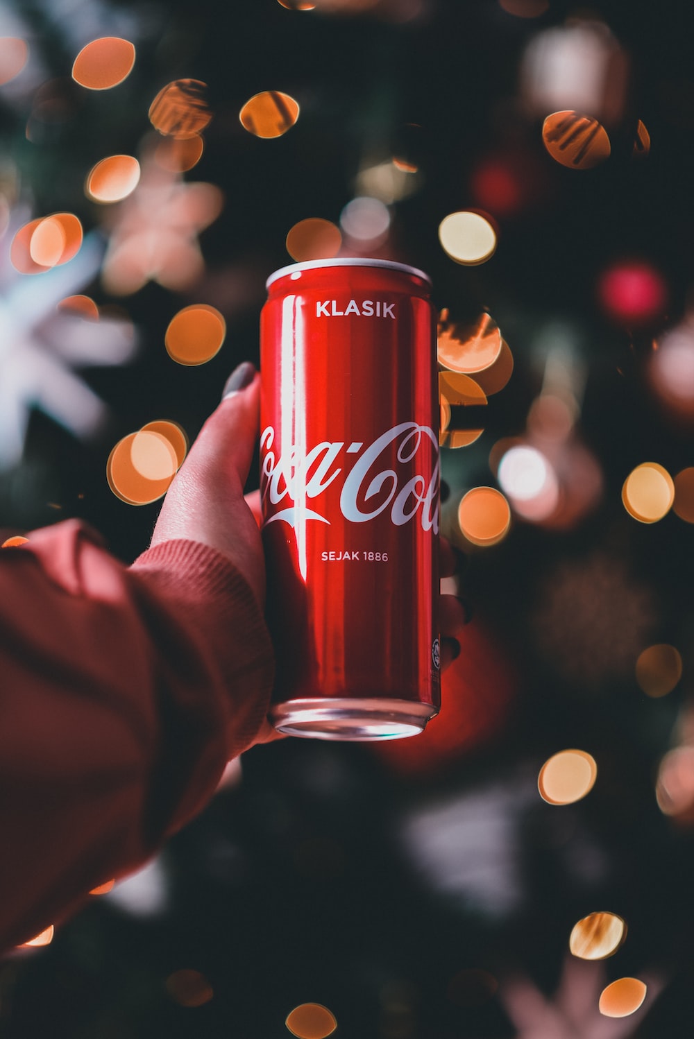A person holding a can of coca cola in front of a christmas tree photo