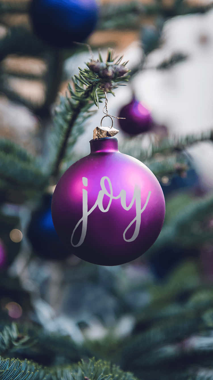 Download A Purple Christmas Ornament With The Word Joy Hanging On It Wallpaper