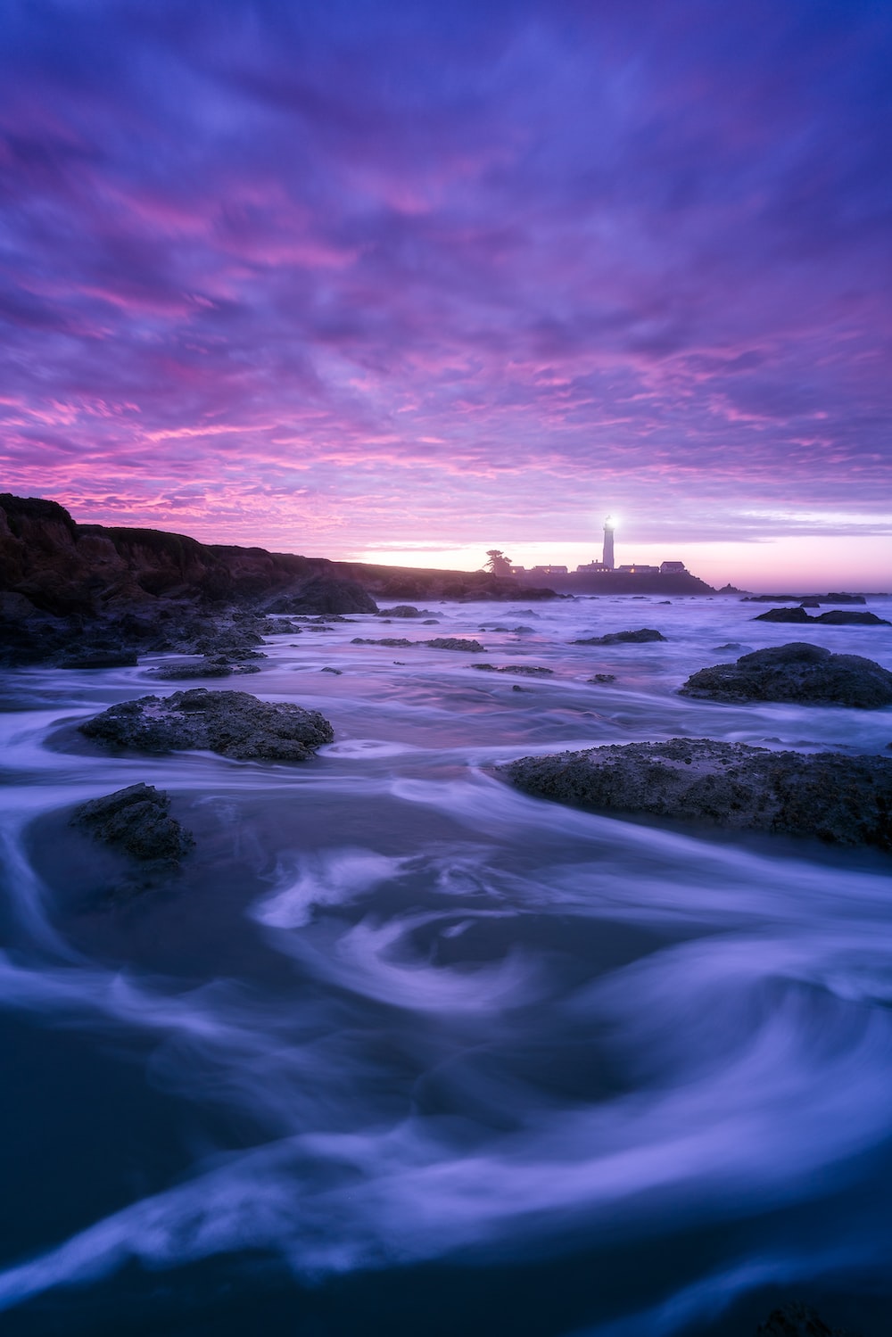 Rocks and sea with silhouette of lighthouse in background photo
