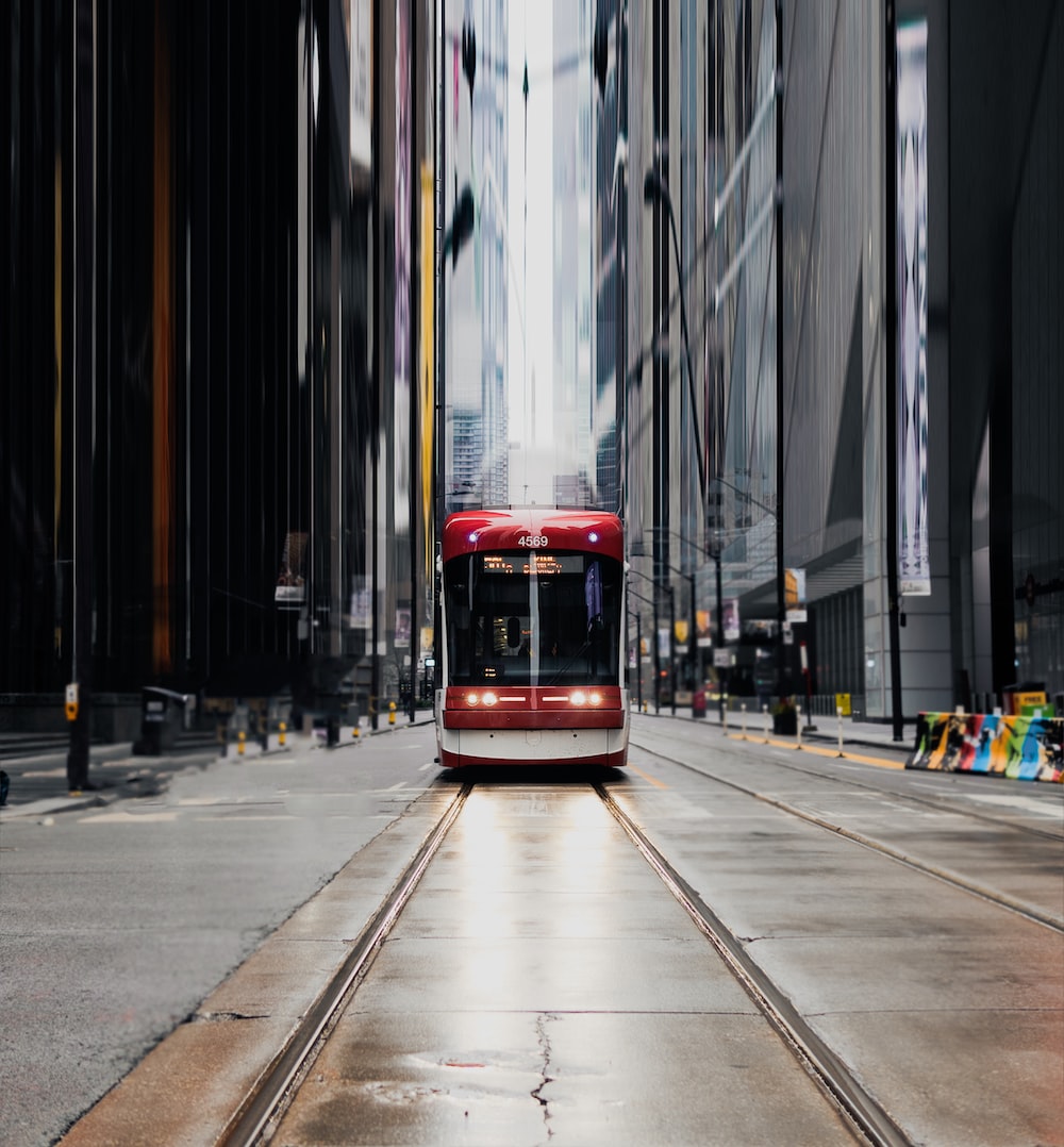 A red and white train traveling down a street next to tall buildings photo