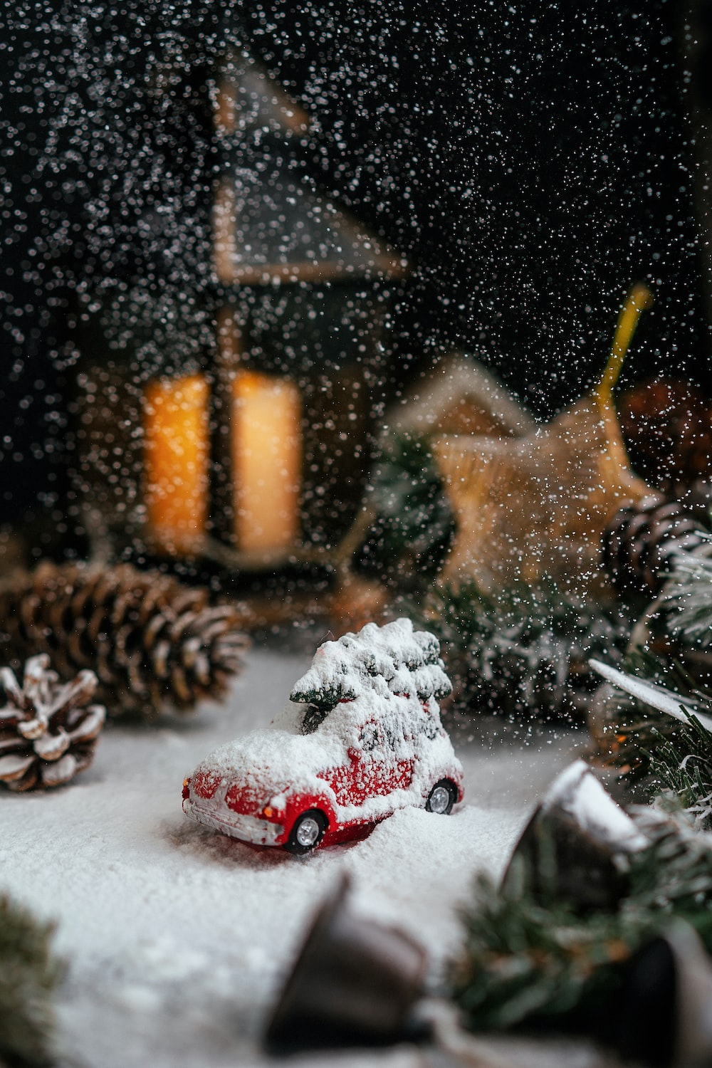A toy car covered in snow next to a christmas tree photo