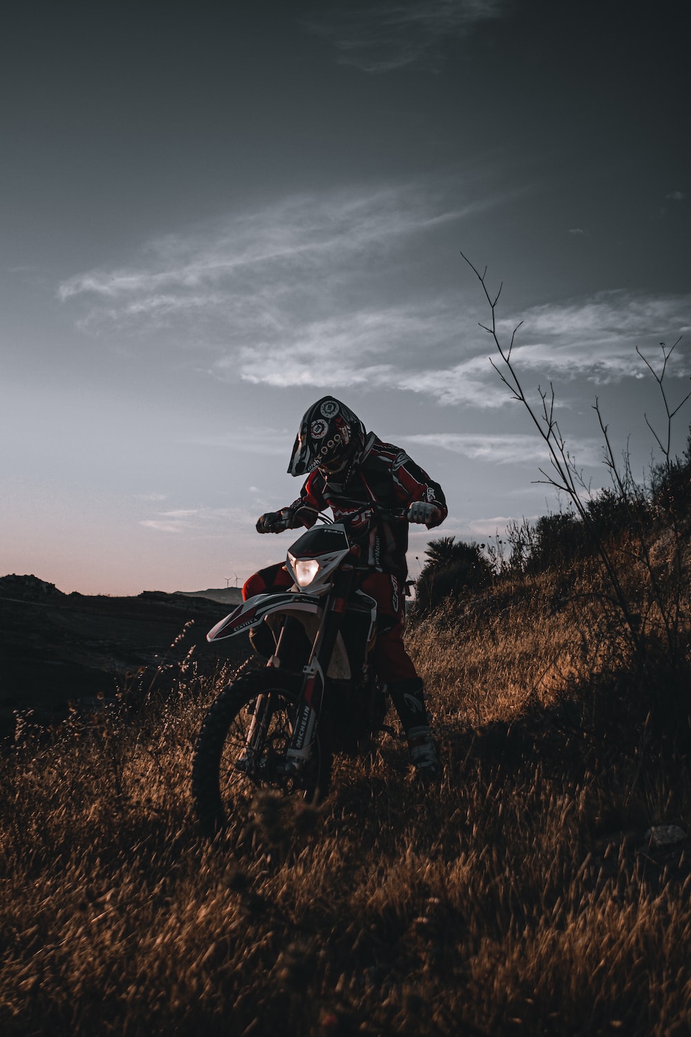 Man in black and red motorcycle suit riding motocross dirt bike on brown grass field during photo
