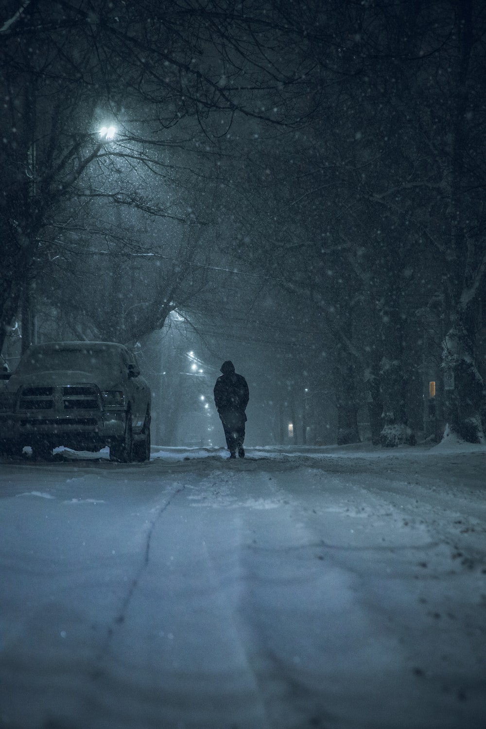 Person in black jacket standing on snow covered road during night time photo