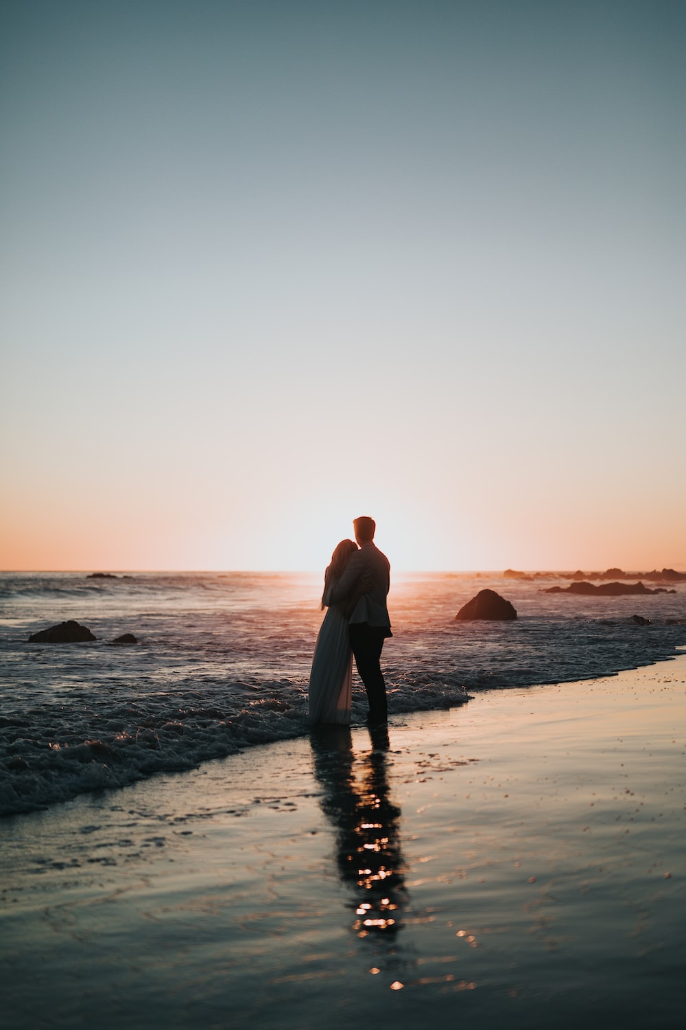 Silhouette photo of couple standing on beach watching sunset photo