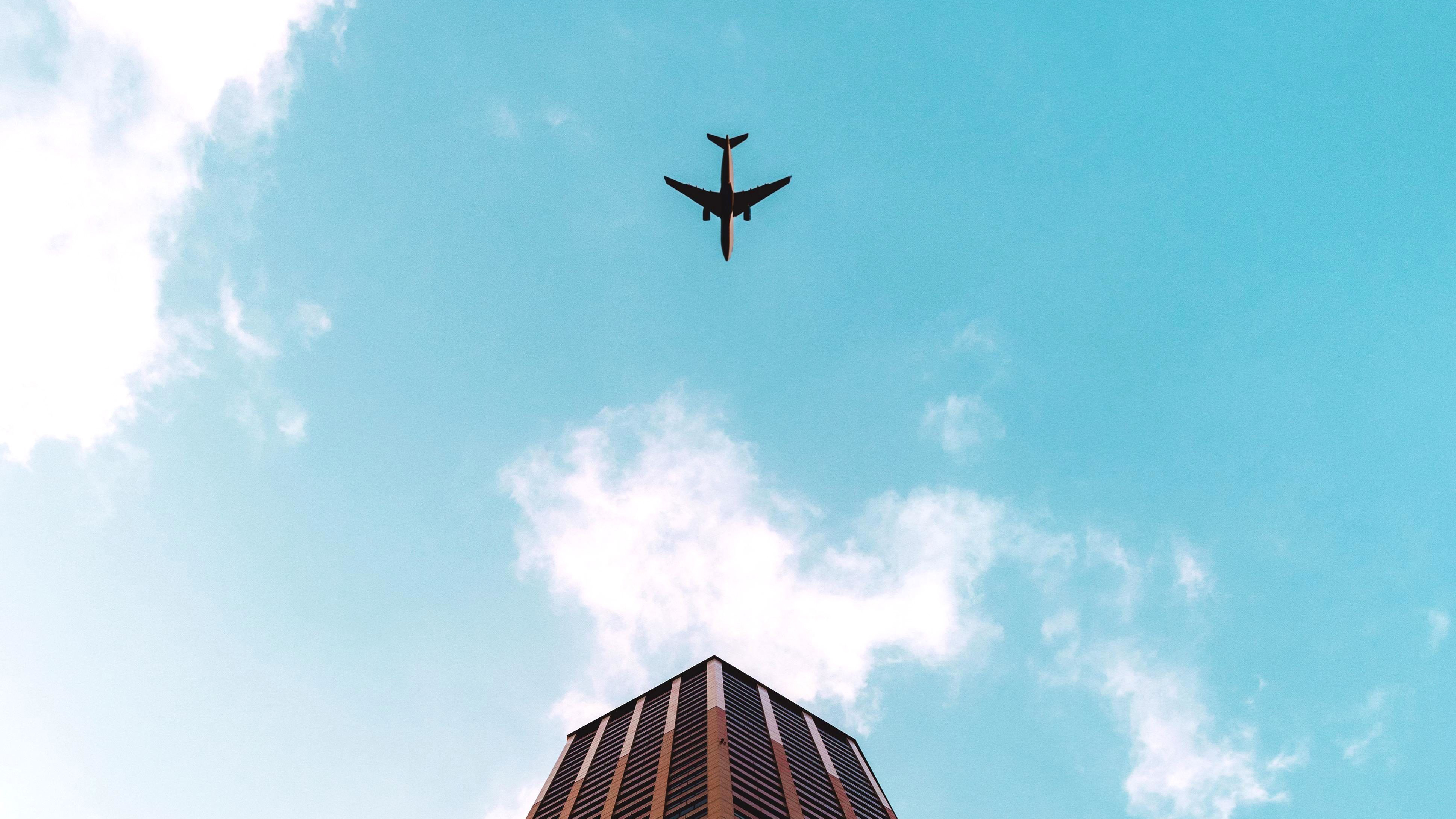 Plane Flying Over Building 4k Wallpaper
