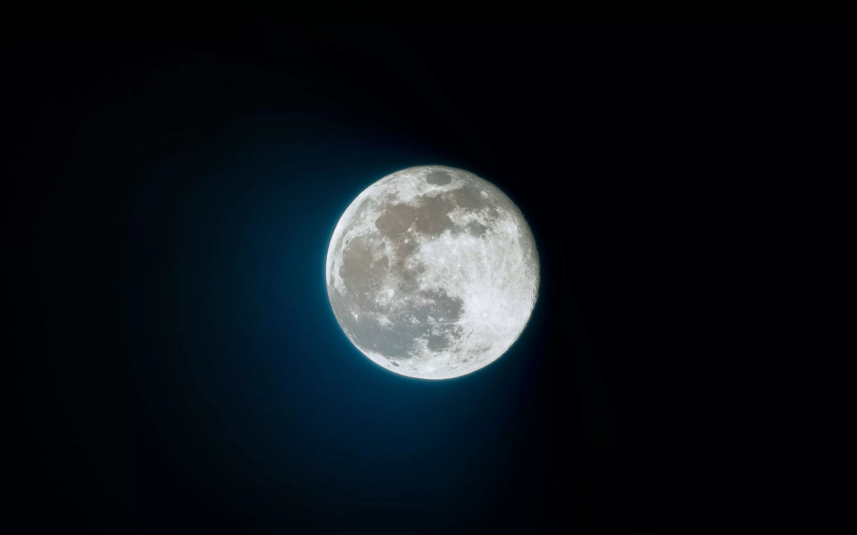 A full moon is seen in the dark sky