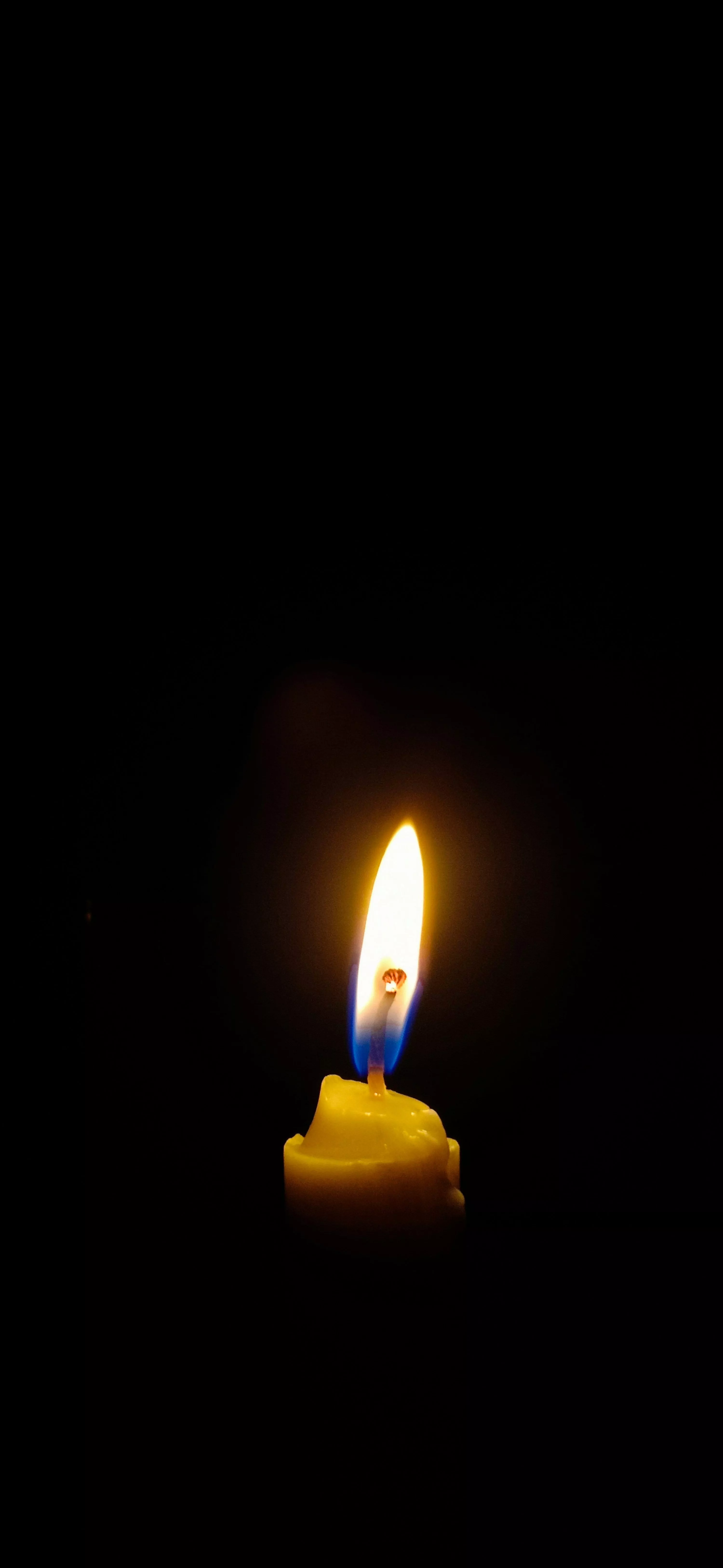 A lit candle in the dark with a black