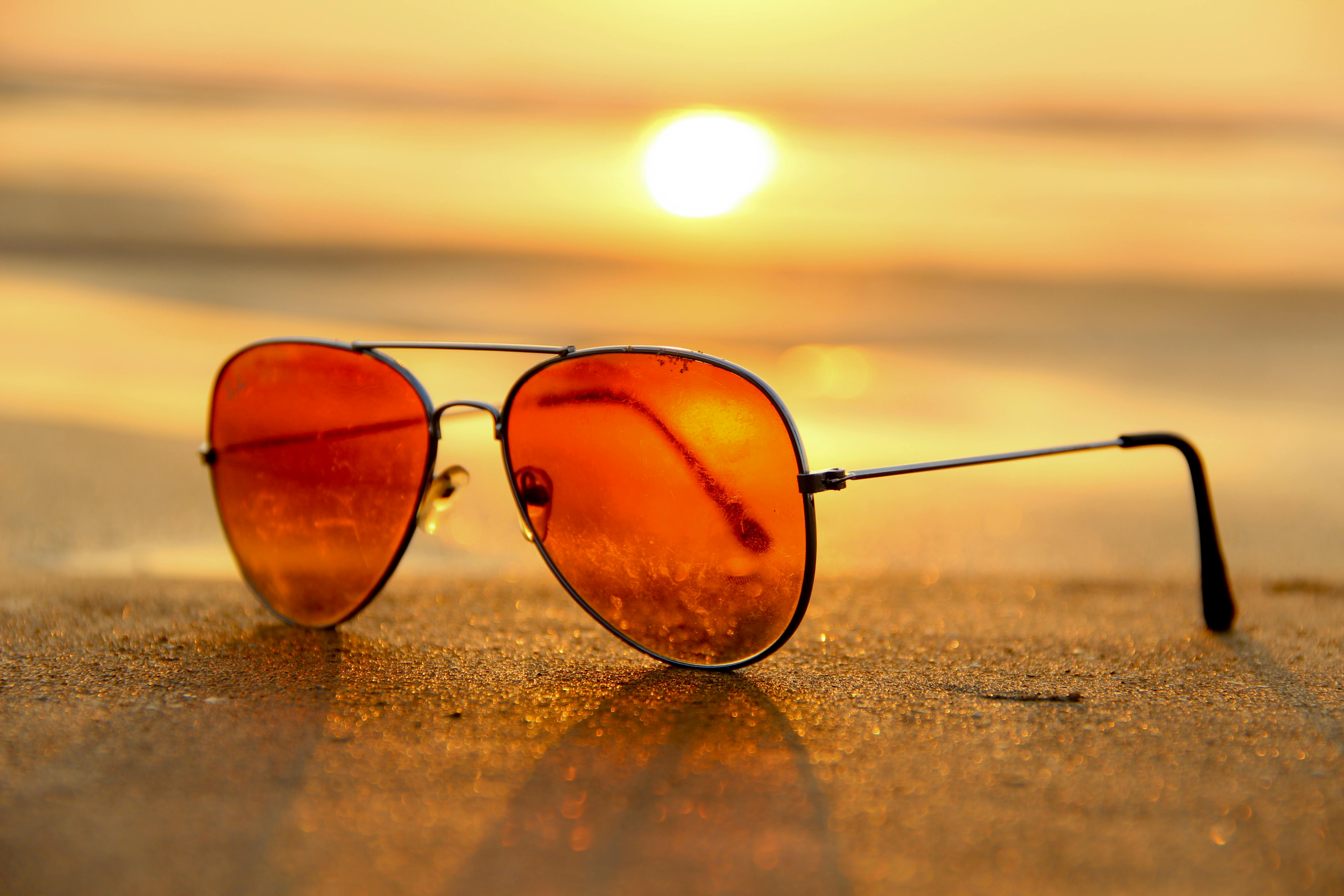 Red Lens Sunglasses on Sand Near Sea at