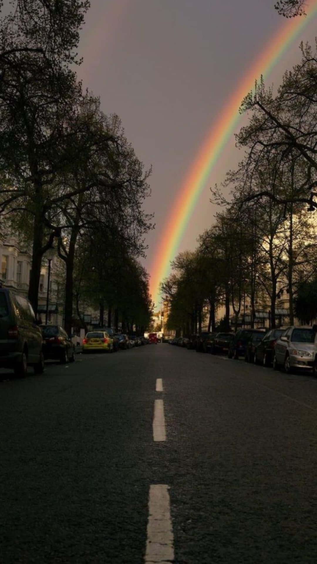 Download A Rainbow Is Seen Over A Street With Cars Parked In The Street Wallpaper