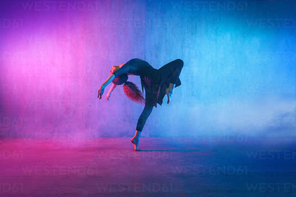 A modern dance girl dancer dancing in neon light doing gymnastic exercises in studio, copy space