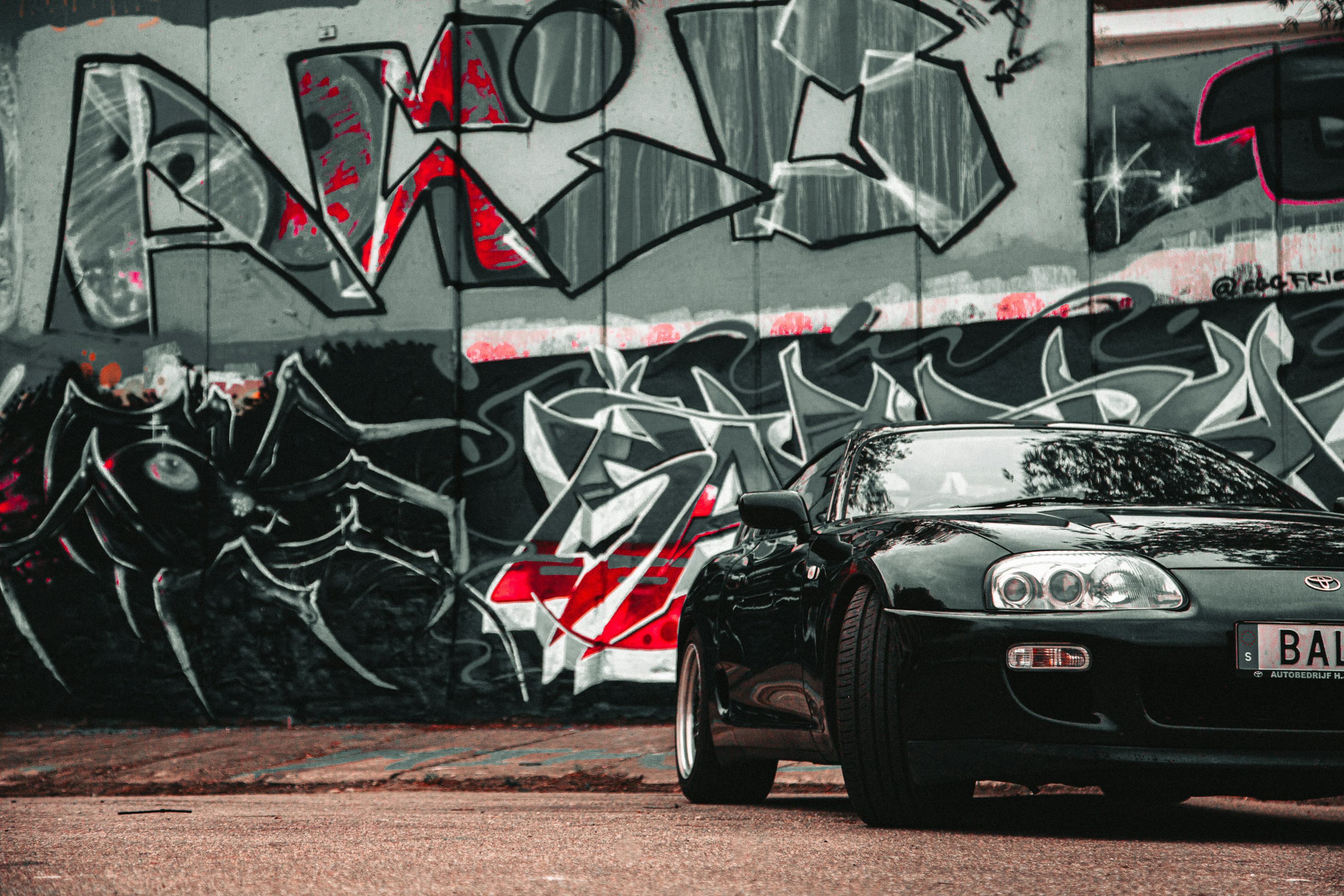 A black sports car parked in front of a graffiti covered wall photo