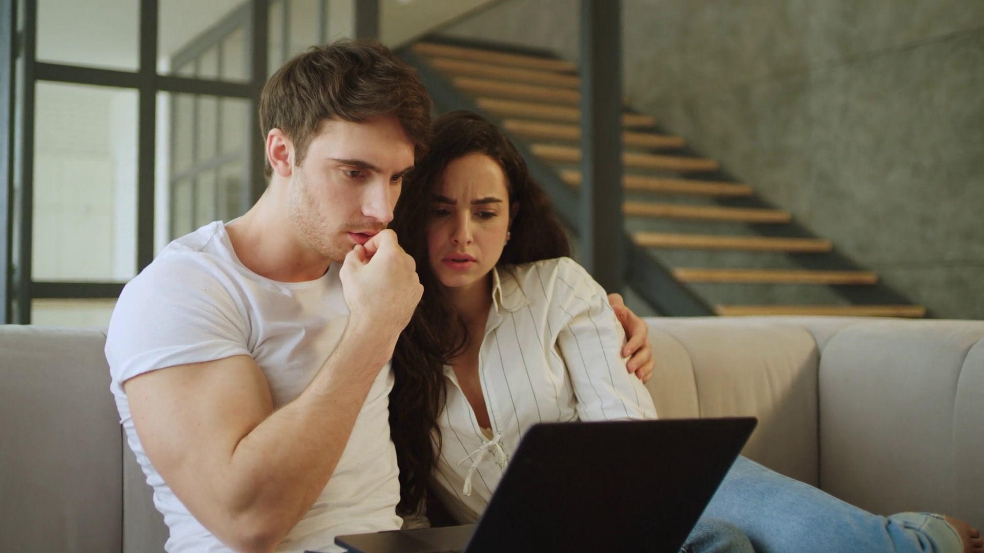 Young married couple watching a suspenseful video on a laptop. Startled man and woman showing fear while viewing. Startled couple watching a thrilling movie on a laptop at home
