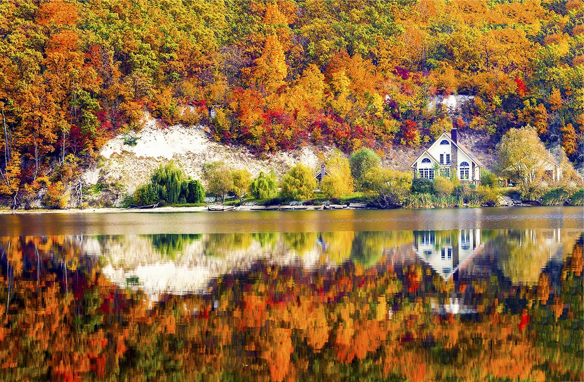 A house on the shore of a lake with trees and a hill®
