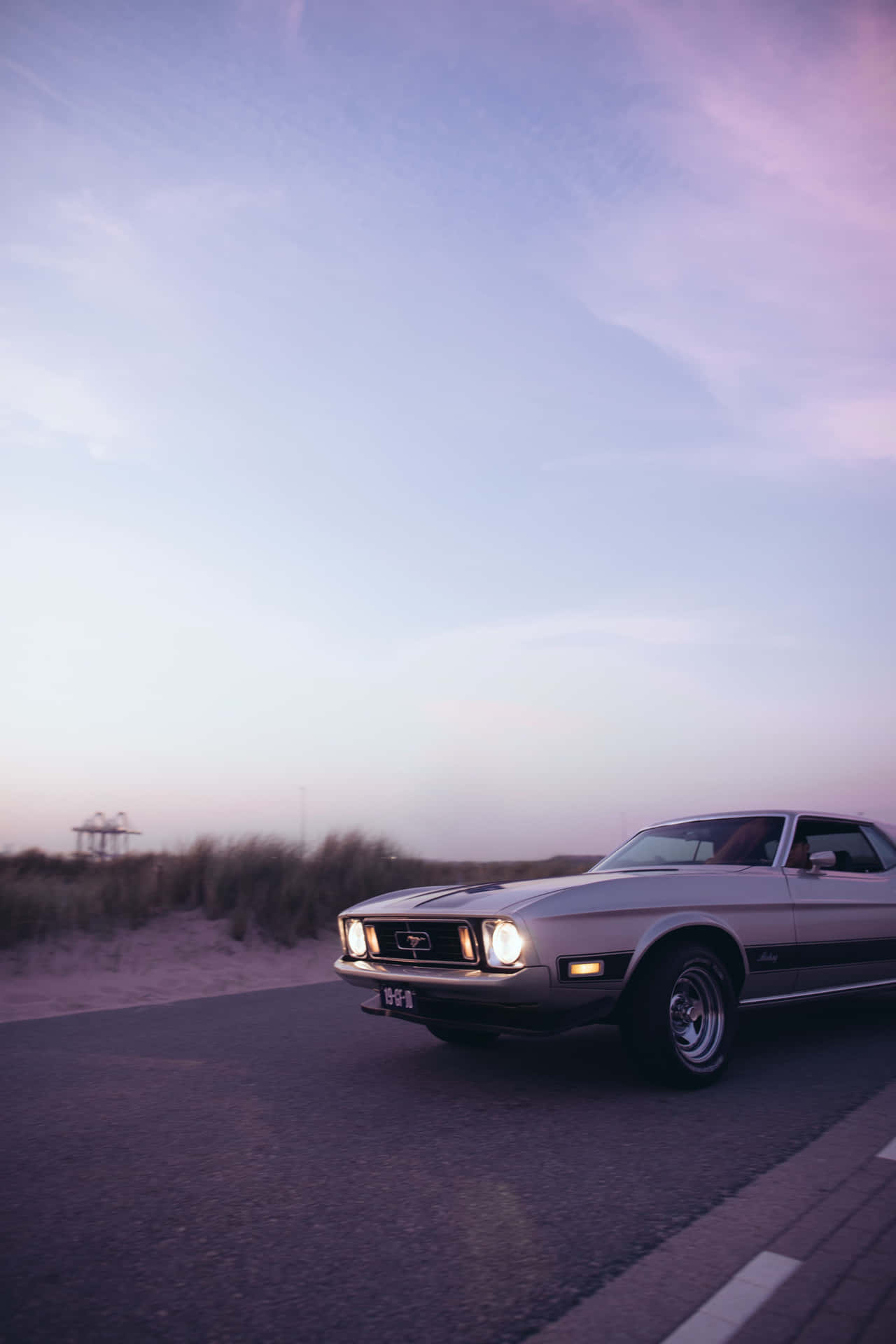 Download A Classic Car Driving Down The Road Wallpaper