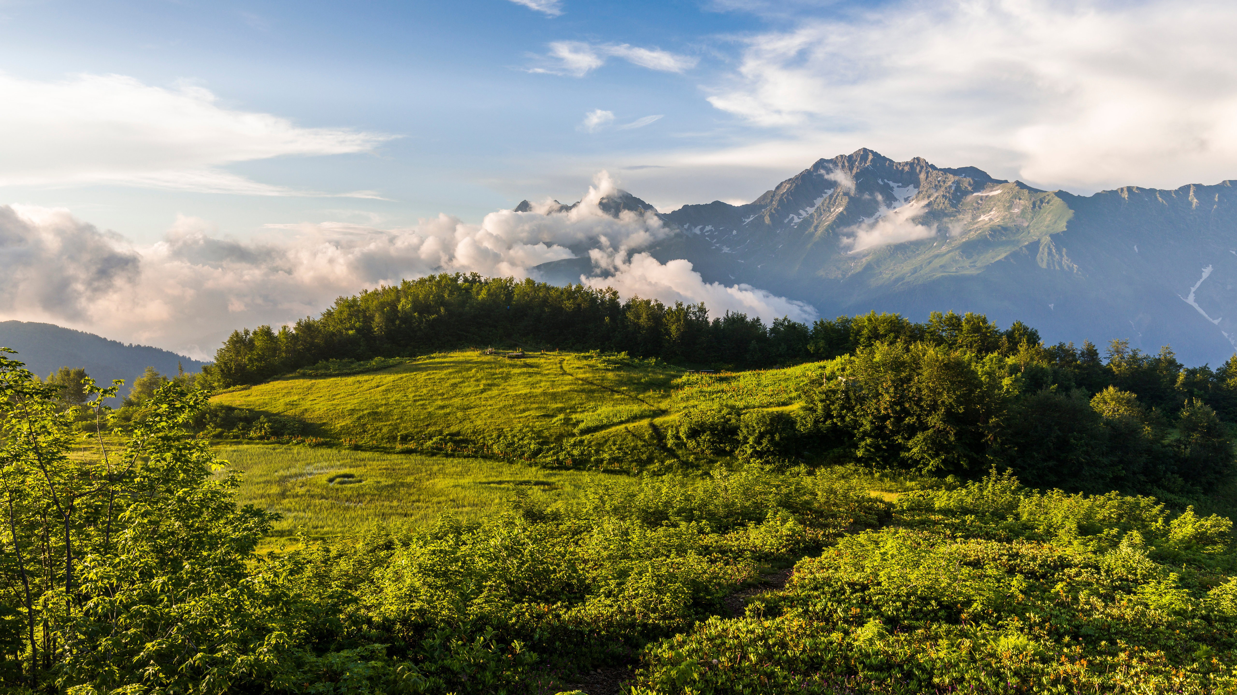 Russia Mountain With Foliage Green Grass And Trees In Background Of Clouds Touching Mountain And Blue Sky 4K 5K HD Nature Wallpaper