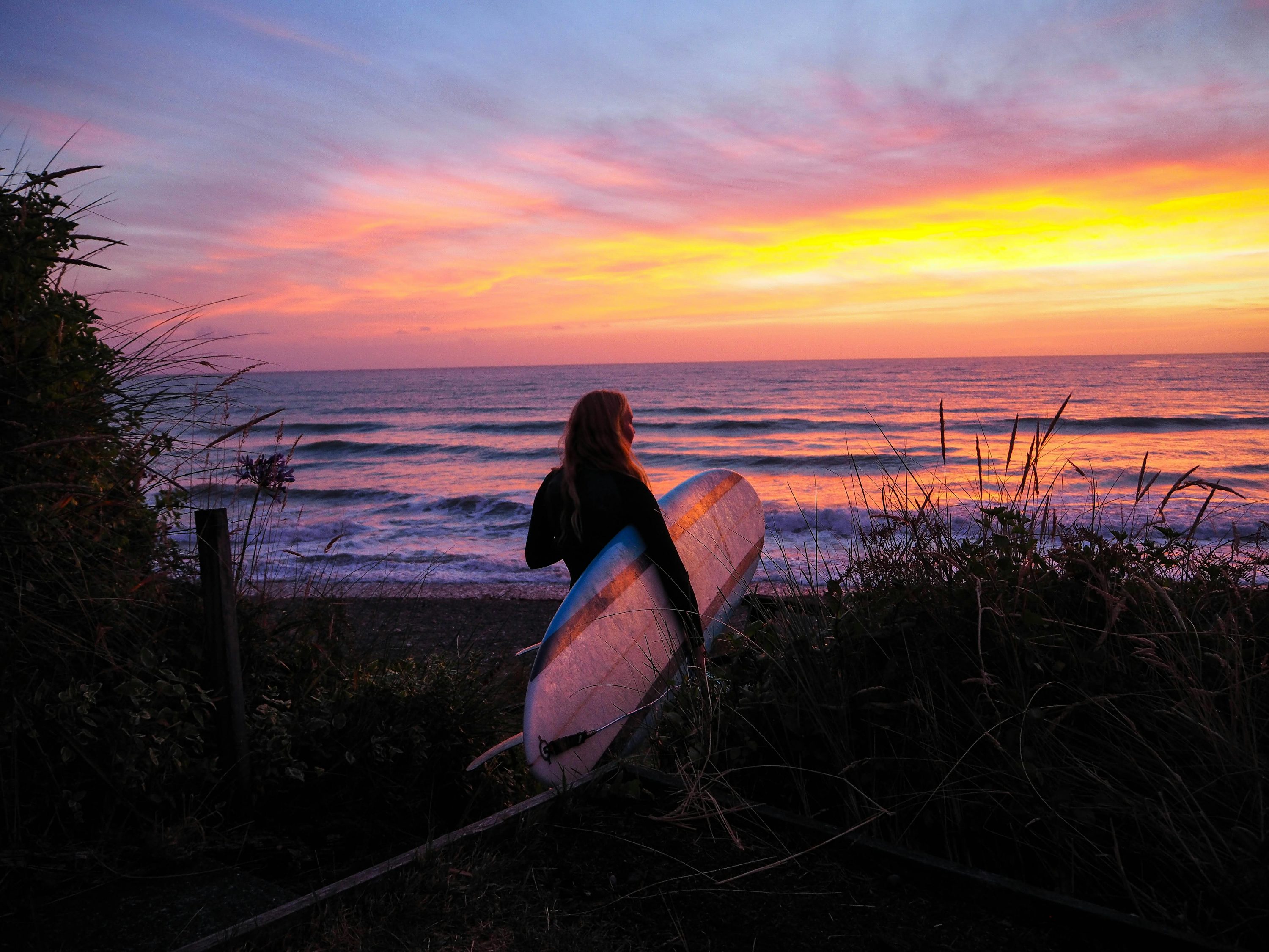 Woman holding surfboard front of the sea during golden hour photo