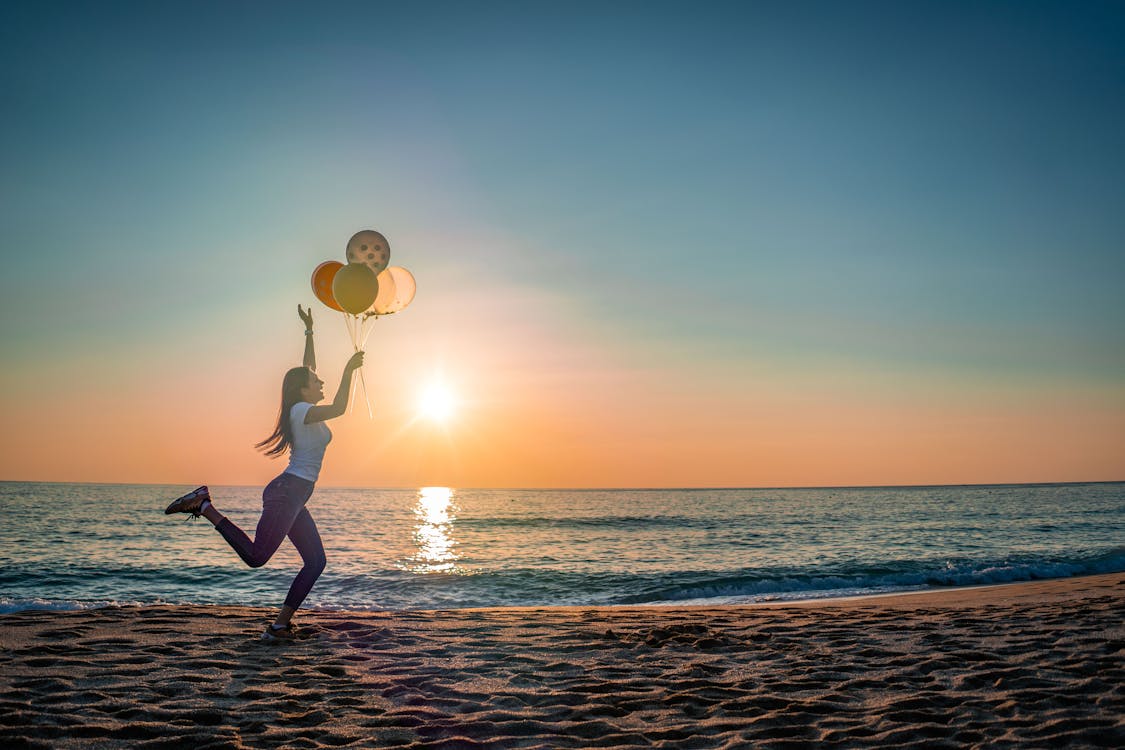 A Woman Holding Balloons at the Beach · Free