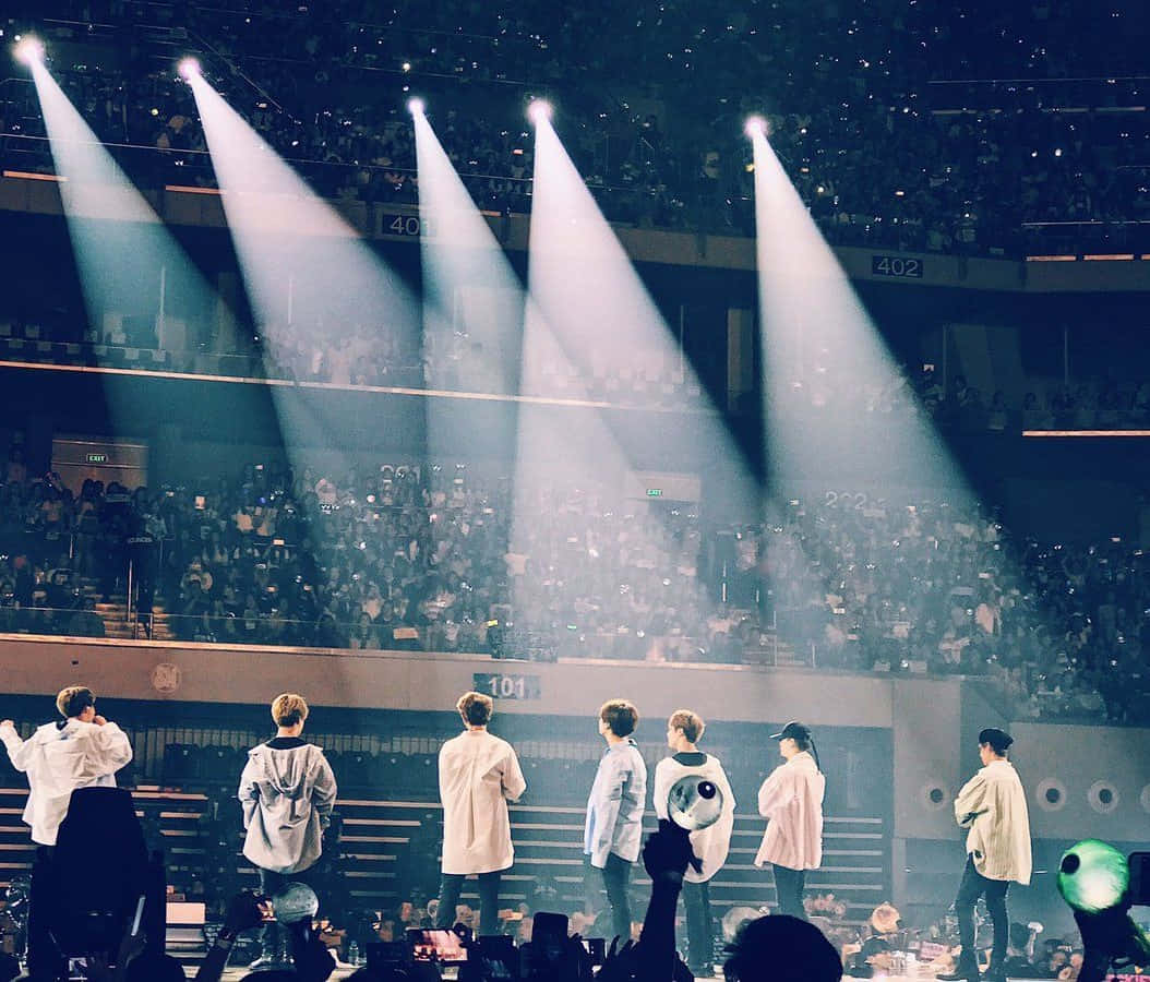 Download BTS performing on stage amidst a mesmerizing light show Wallpaper