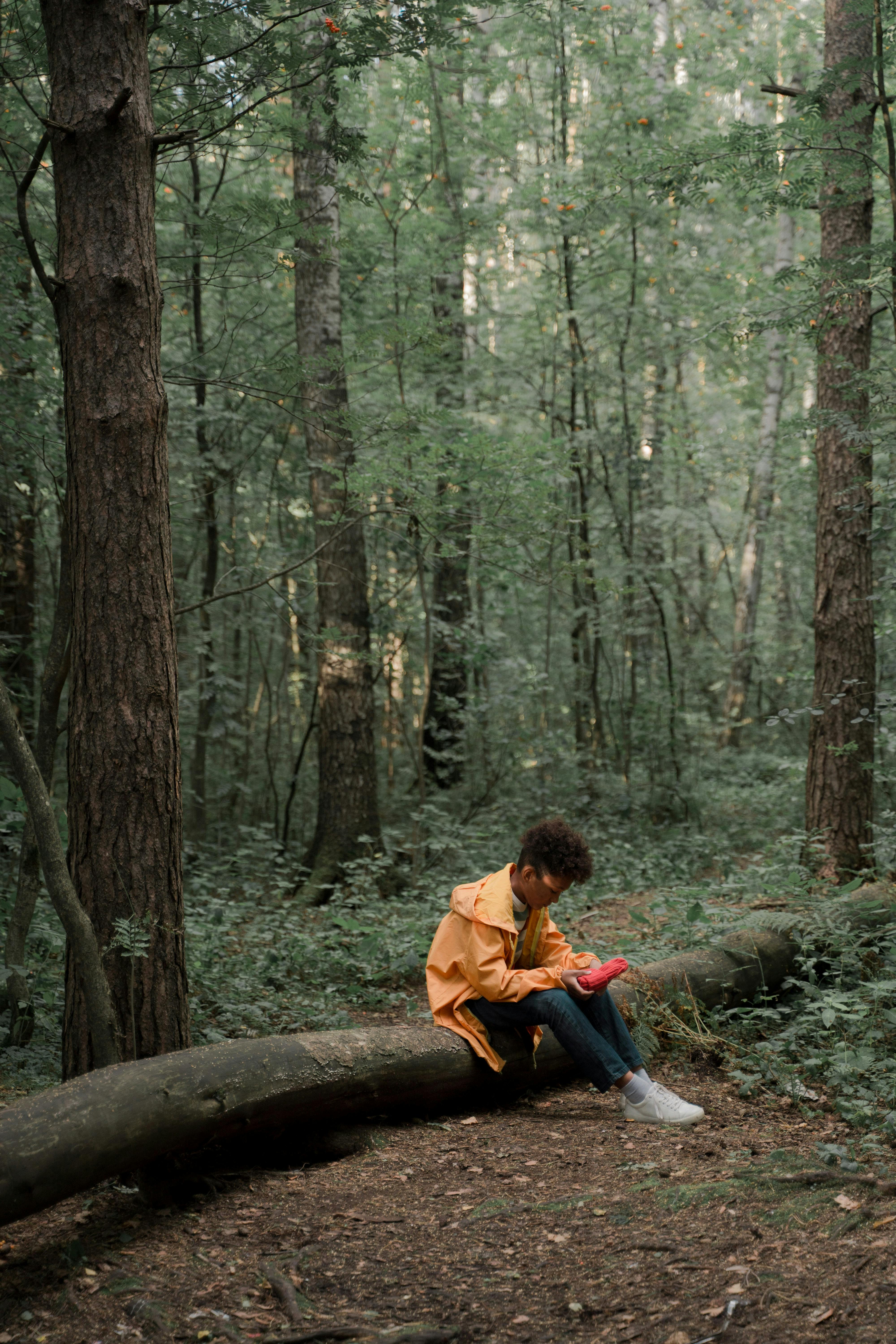 Sad Teenage Boy in Yellow Raincoat Sitting on Log in Forest · Free