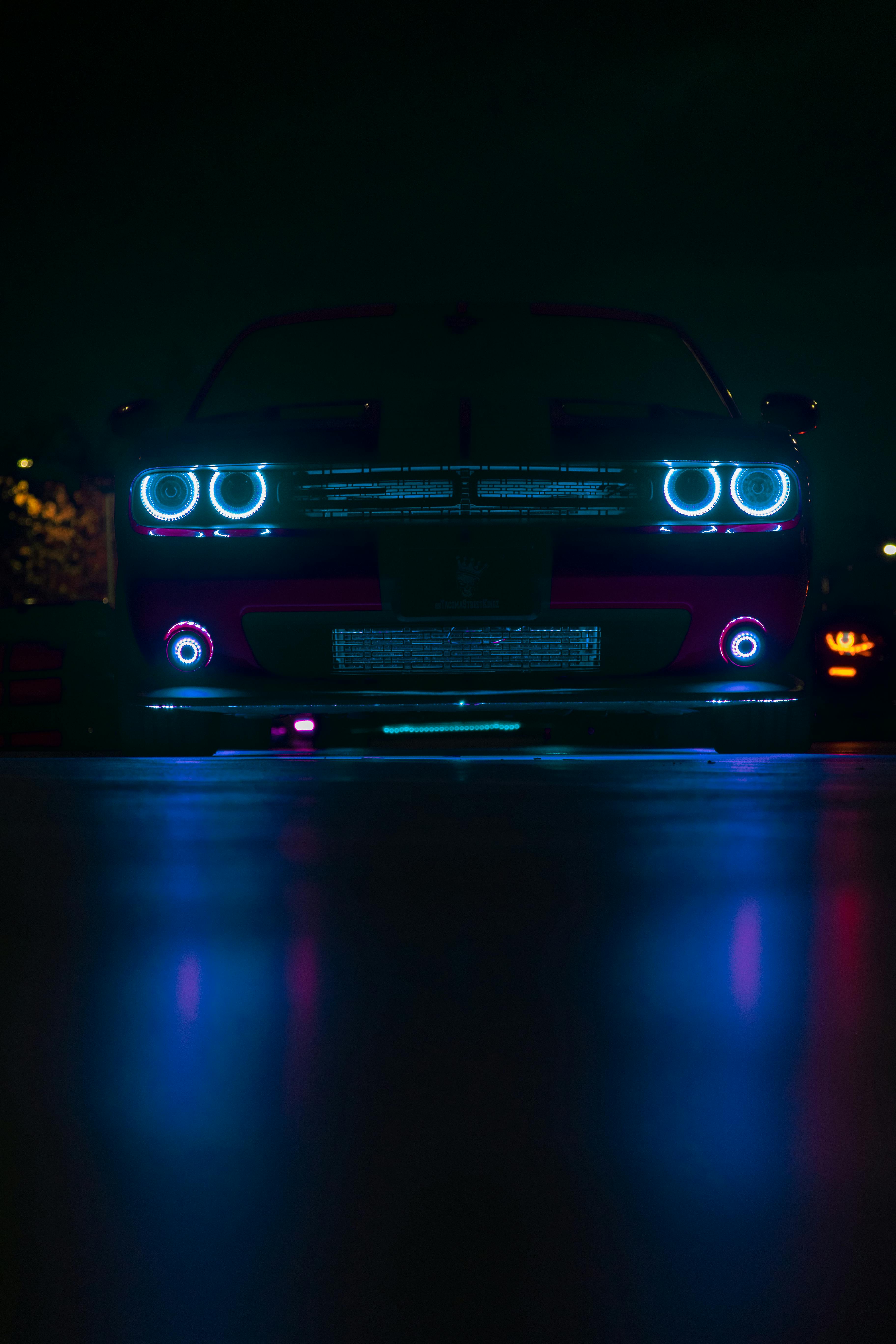 Dodge Challenger with Blue Headlights Reflecting in the Street Surface at Night · Free