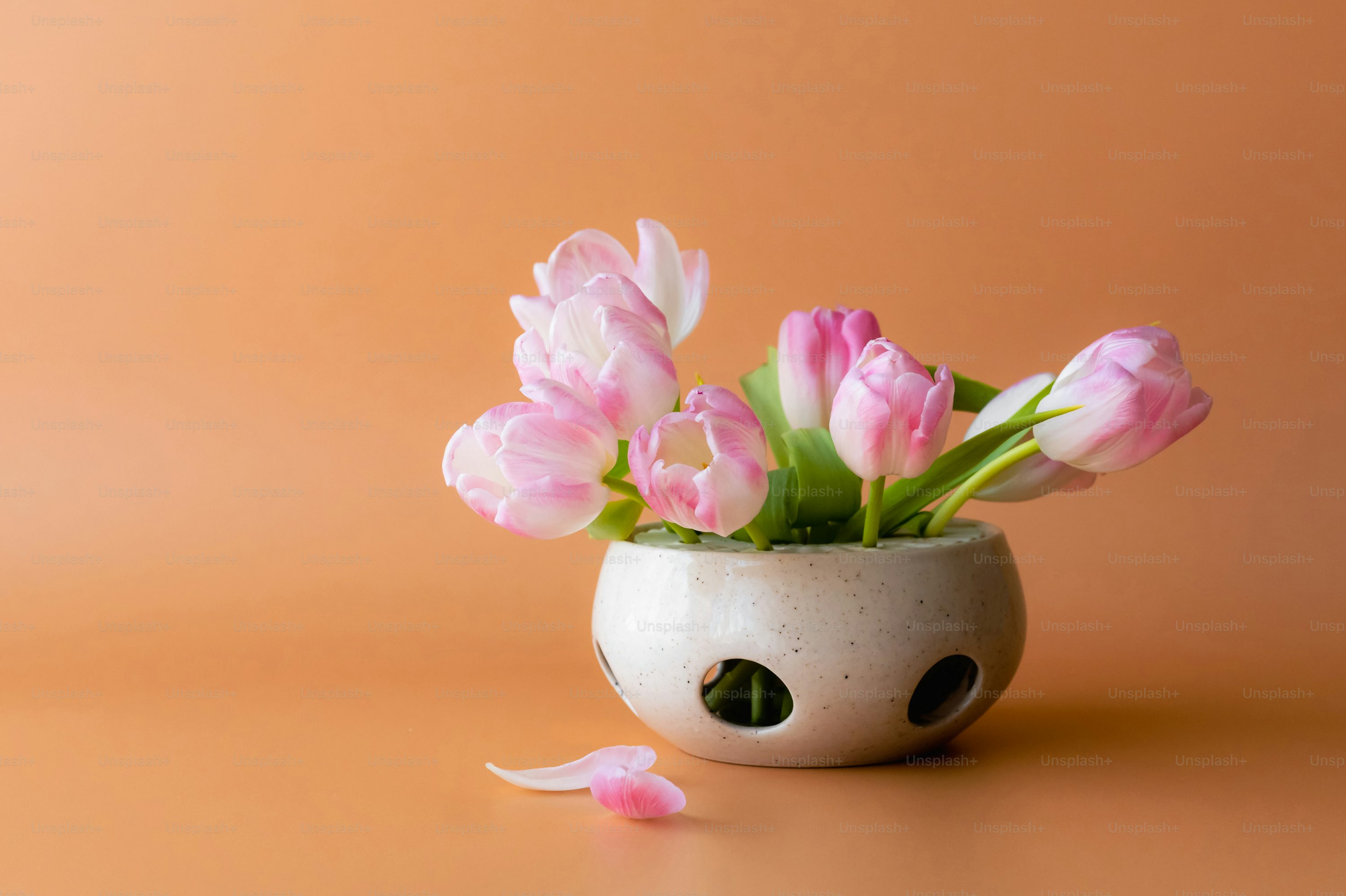 A white vase filled with pink flowers on top of a table photo